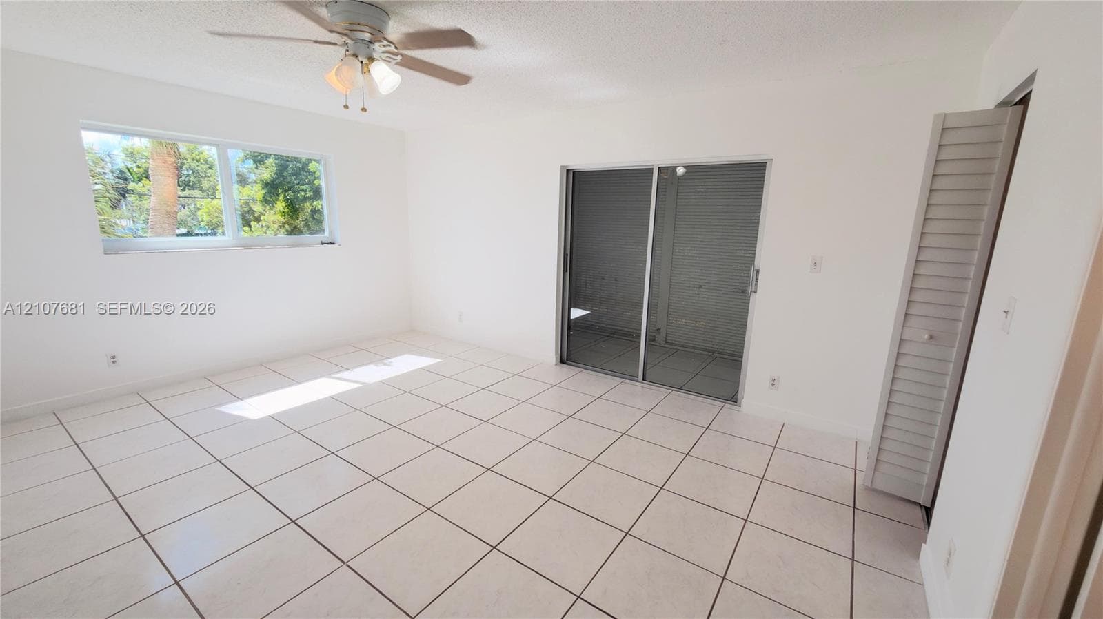 Ceramic tile flooring, sliding glass door, ceiling fan with integrated lighting, and louvered closet doors