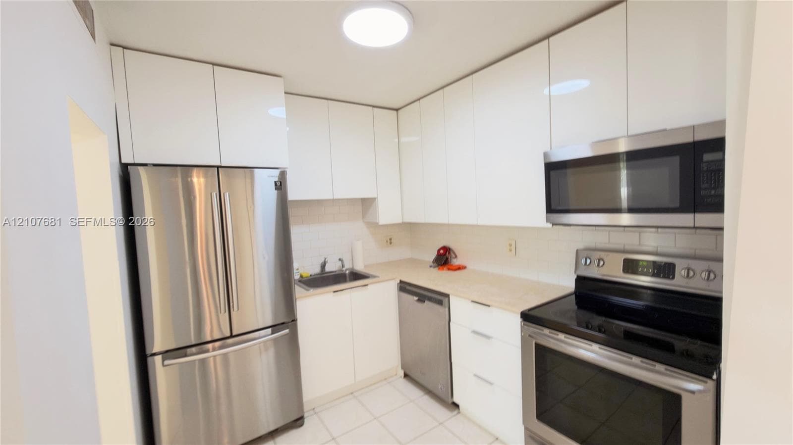 Kitchen featuring high-gloss white cabinetry, stainless steel appliances, light-toned countertops, subway tile backsplash, and tile flooring