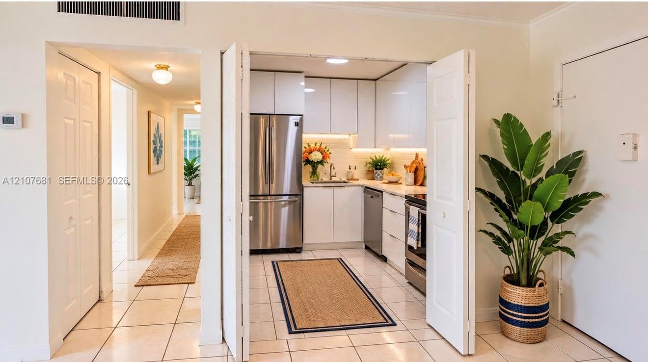 Kitchen featuring white flat-panel cabinetry, stainless steel appliances, solid-surface countertops, under-cabinet lighting, and tile flooring