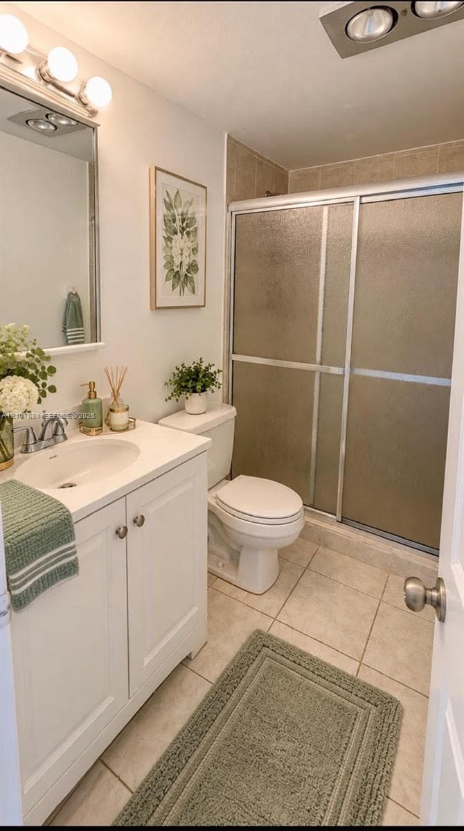 Bathroom featuring a white vanity cabinet with a solid surface countertop, an oval undermount sink, a chrome faucet, a shower enclosure with sliding glass doors, and tiled flooring