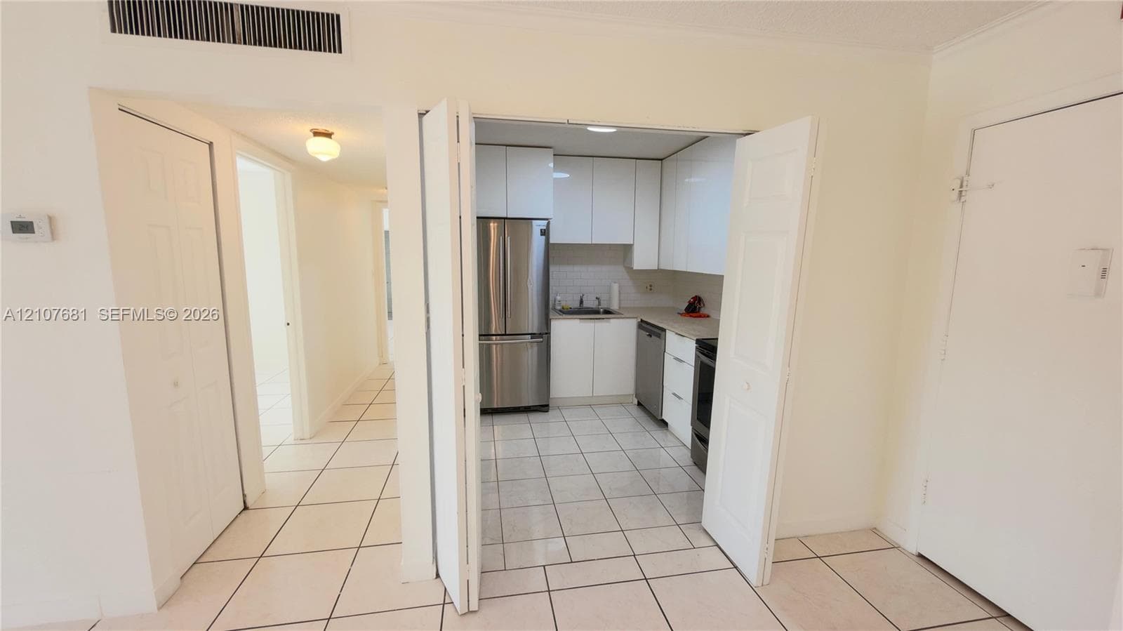 Kitchen featuring high-gloss white cabinetry, stainless steel appliances, ceramic tile flooring, and solid-surface countertops
