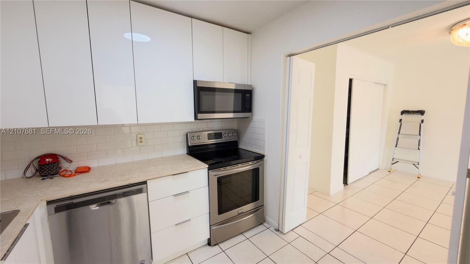 Kitchen featuring flat-panel white cabinetry, stainless steel appliances, subway tile backsplash, and light-toned countertops