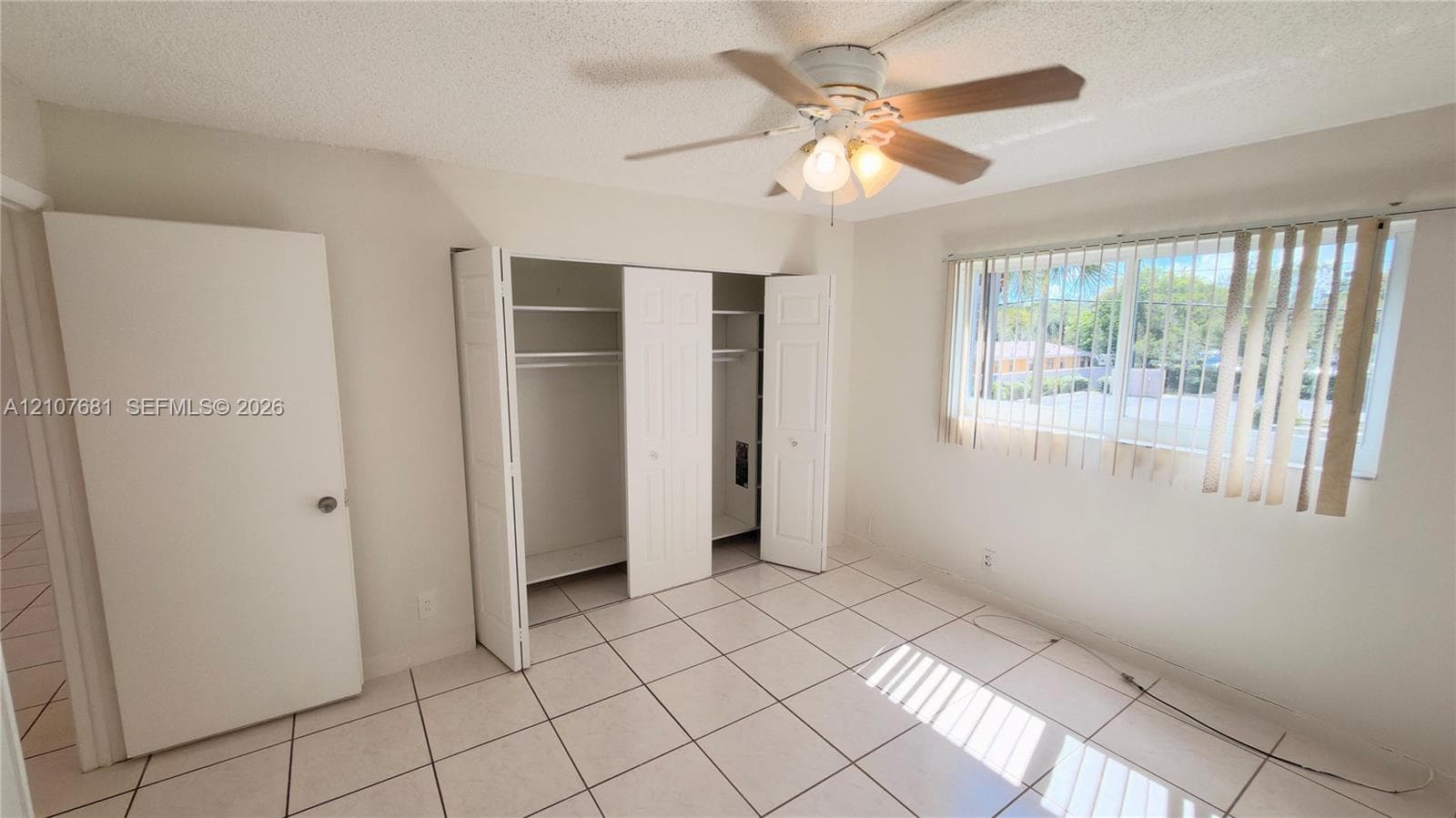 Light-filled room featuring large-format tile flooring, a multi-panel closet with built-in shelving, and a ceiling fan with integrated lighting