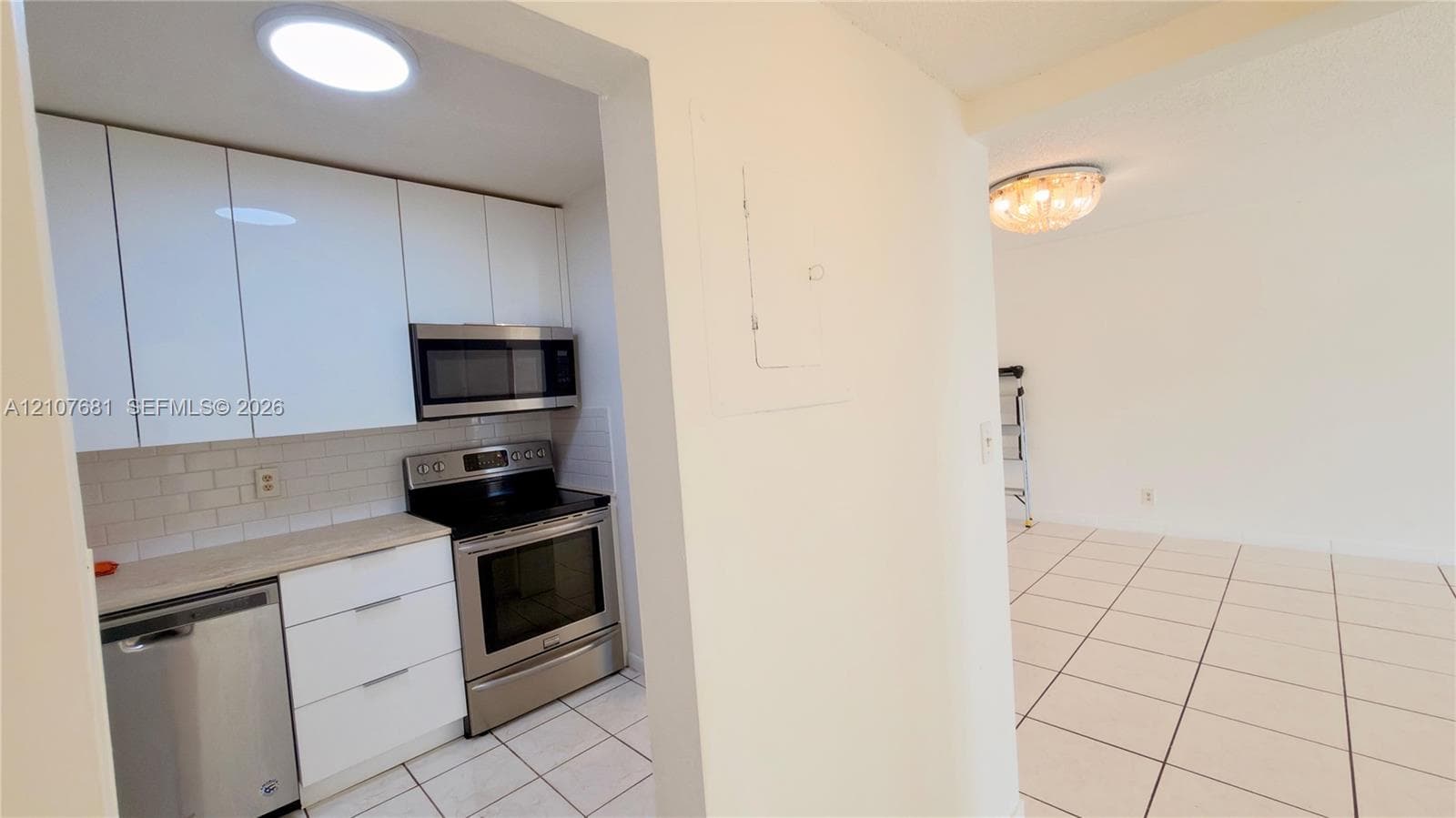 Kitchen featuring white flat-panel cabinetry, light-toned countertops, subway tile backsplash, and stainless steel appliances, including an over-the-range microwave and electric range