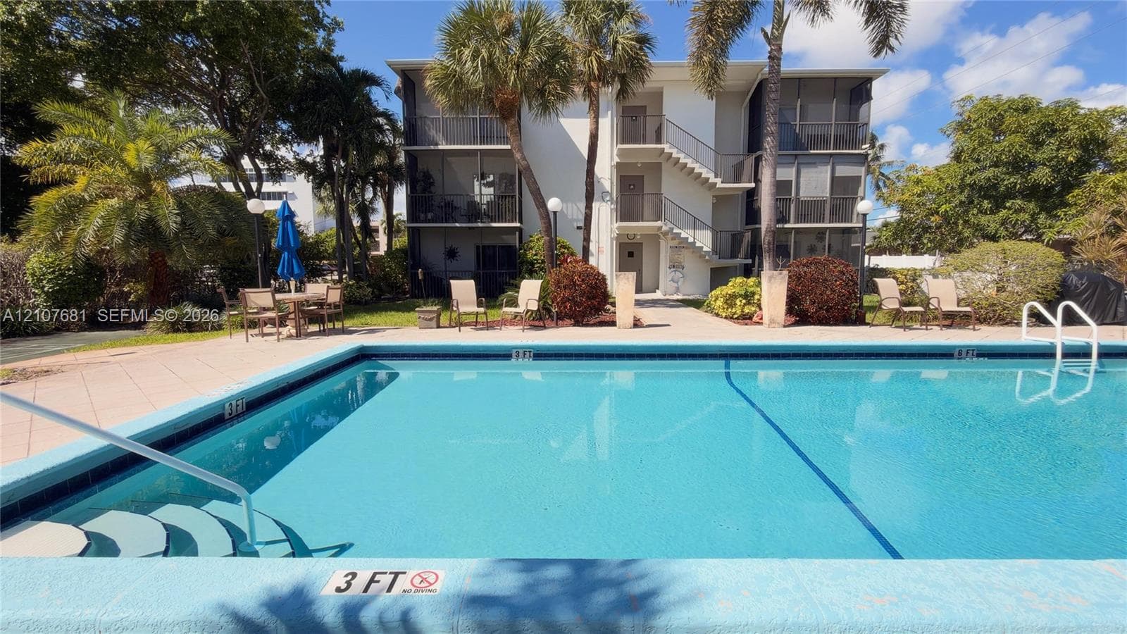 In-ground swimming pool featuring a tiled deck, stair entry, and metal handrails, set against a multi-story exterior with screened balconies