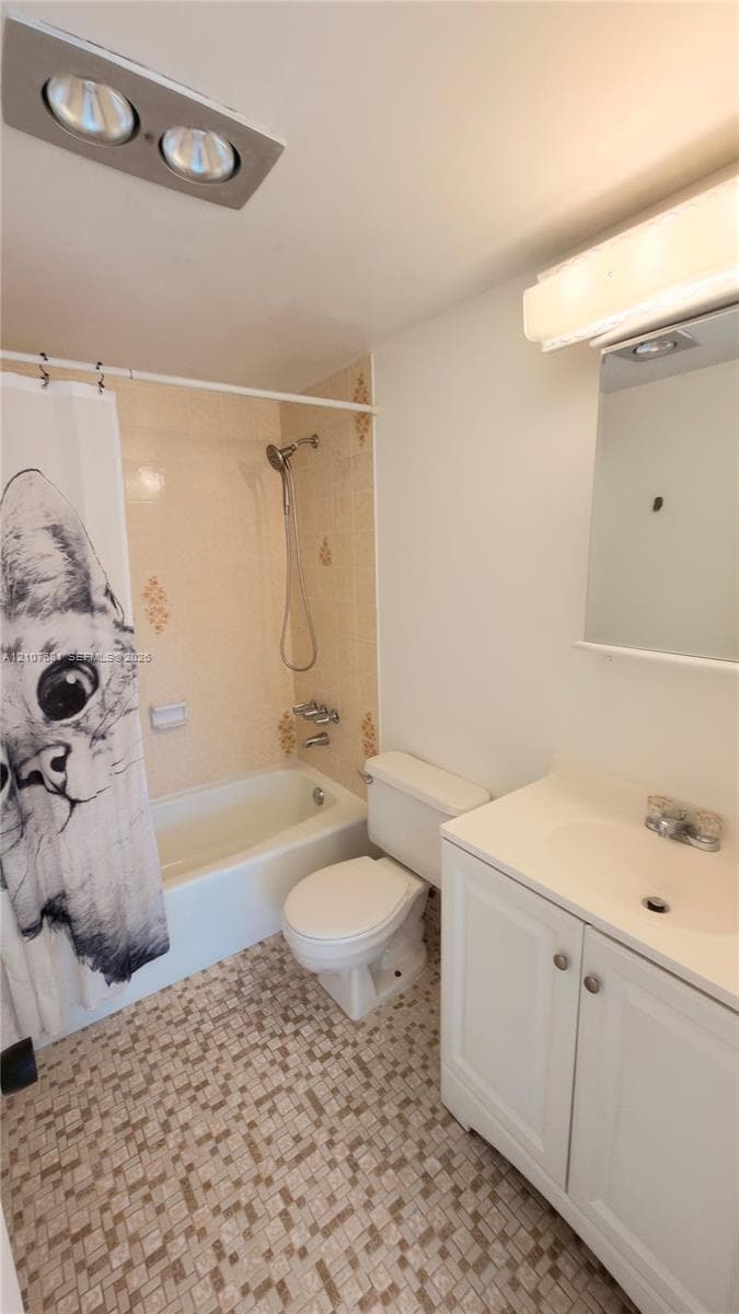 Bathroom featuring a white vanity cabinet with a molded sink basin, wall-mounted mirror, ceiling-mounted heating unit, and patterned tile flooring