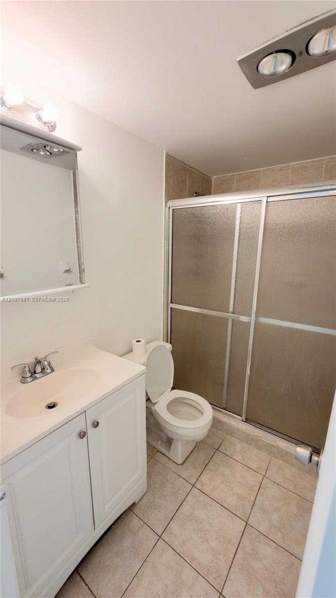 Bathroom featuring white shaker-style cabinetry, an integrated sink with polished chrome hardware, tiled flooring, and a walk-in shower with sliding glass doors