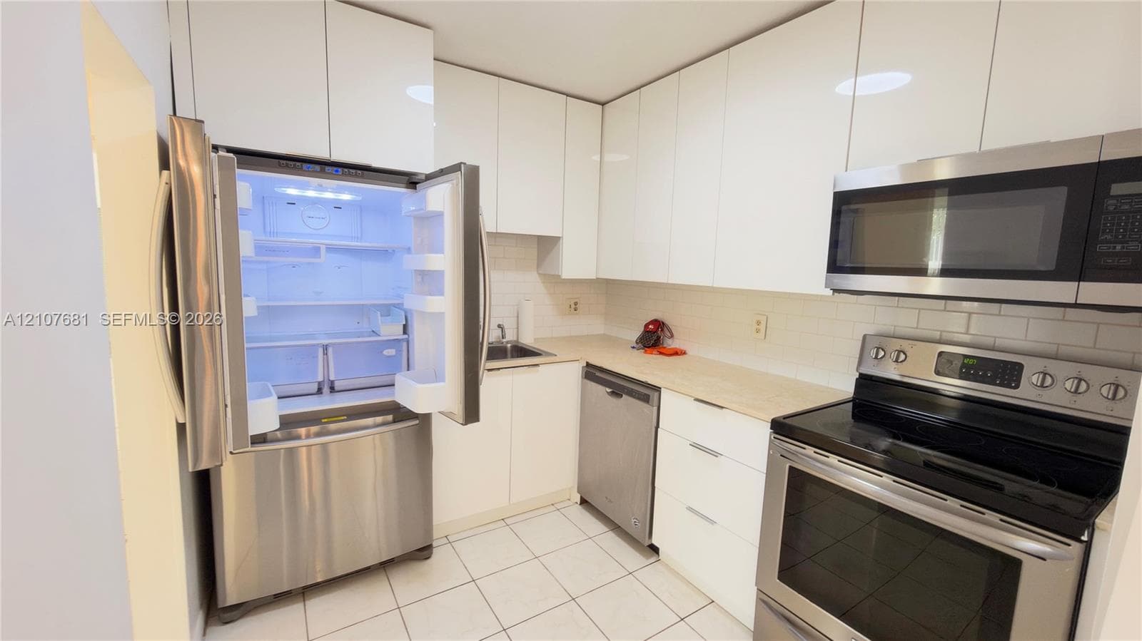 Kitchen featuring flat-panel white cabinetry, stainless steel appliances, light-toned countertops, subway tile backsplash, and tile flooring