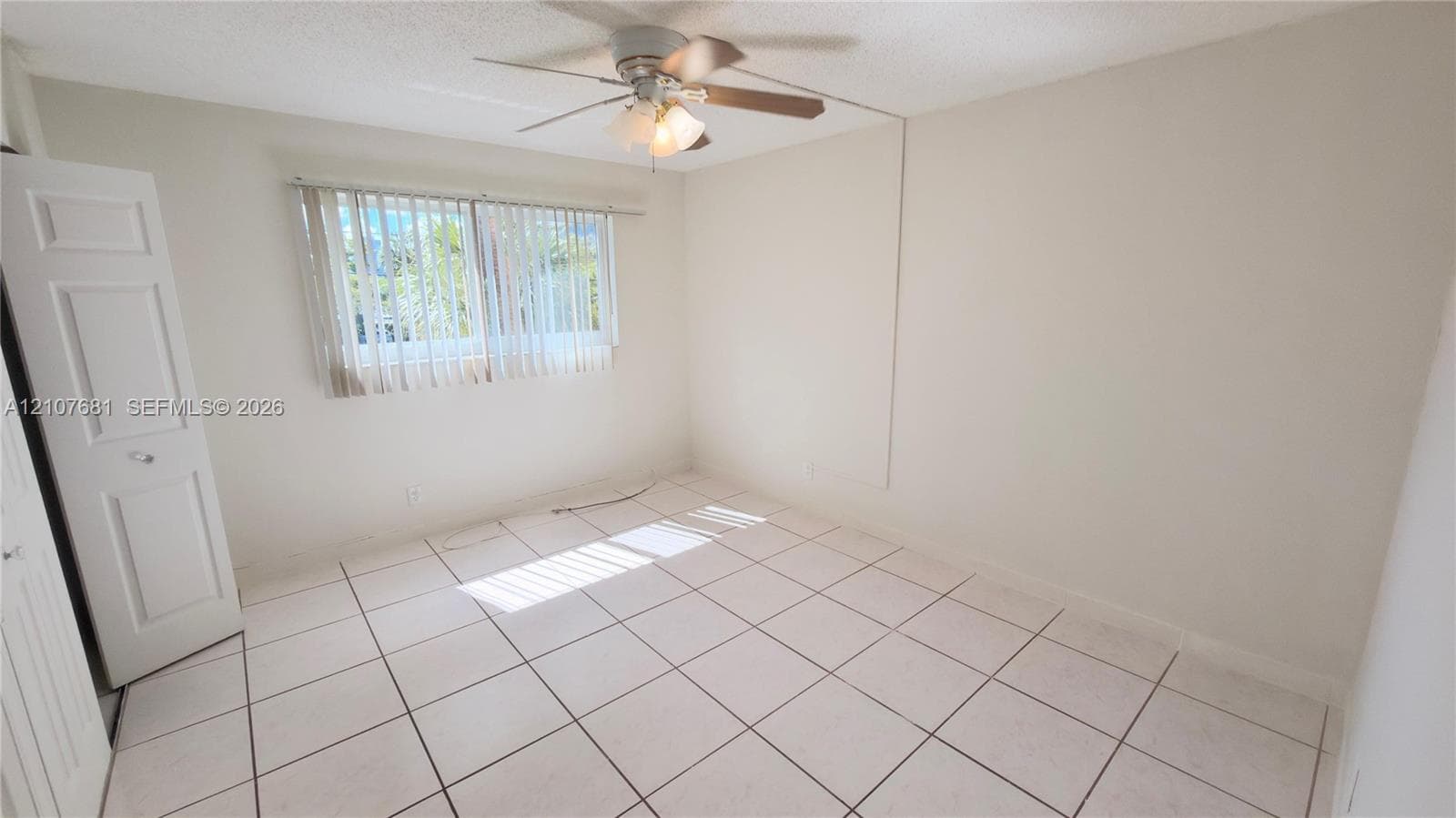 Neutral-toned room featuring tile flooring, a multi-blade ceiling fan with integrated lighting, and vertical window blinds