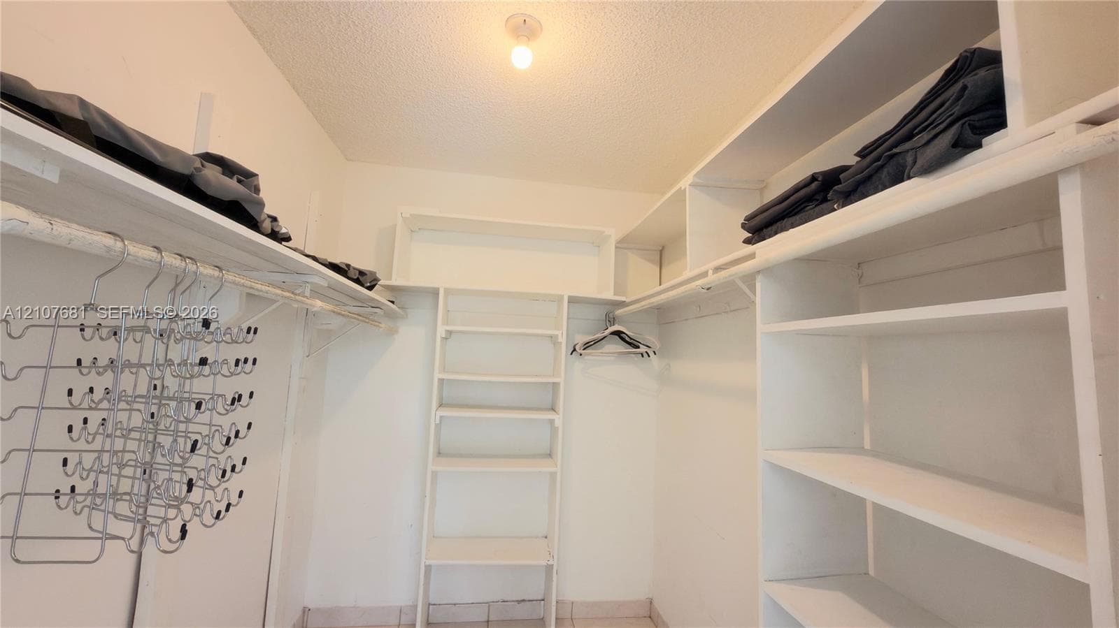Walk-in closet featuring white built-in shelving, overhead storage racks, integrated hanging rods, and tile flooring