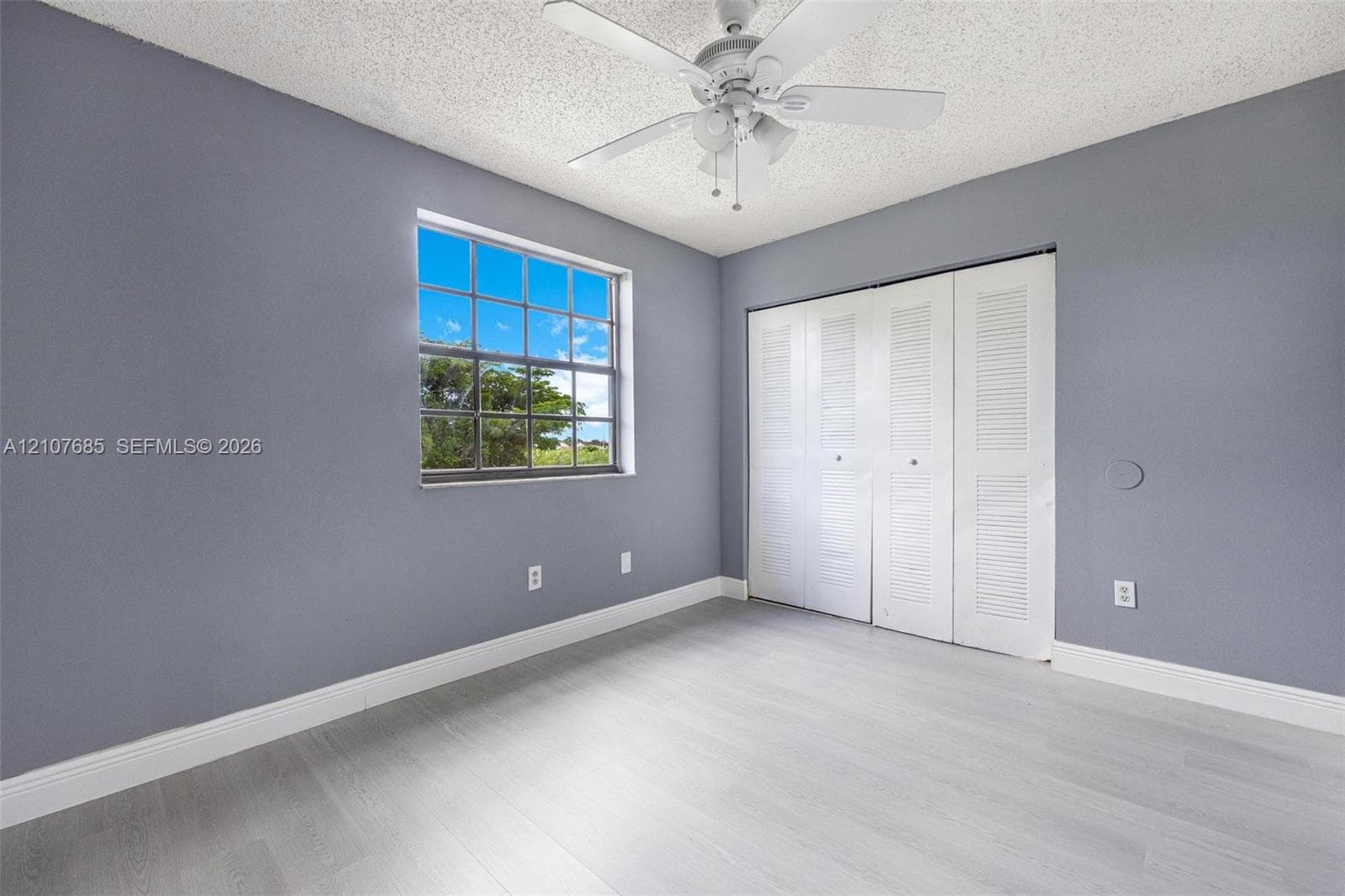 Room featuring wood-finish flooring, white louvered-style closet doors, a multi-pane window, and a ceiling fan