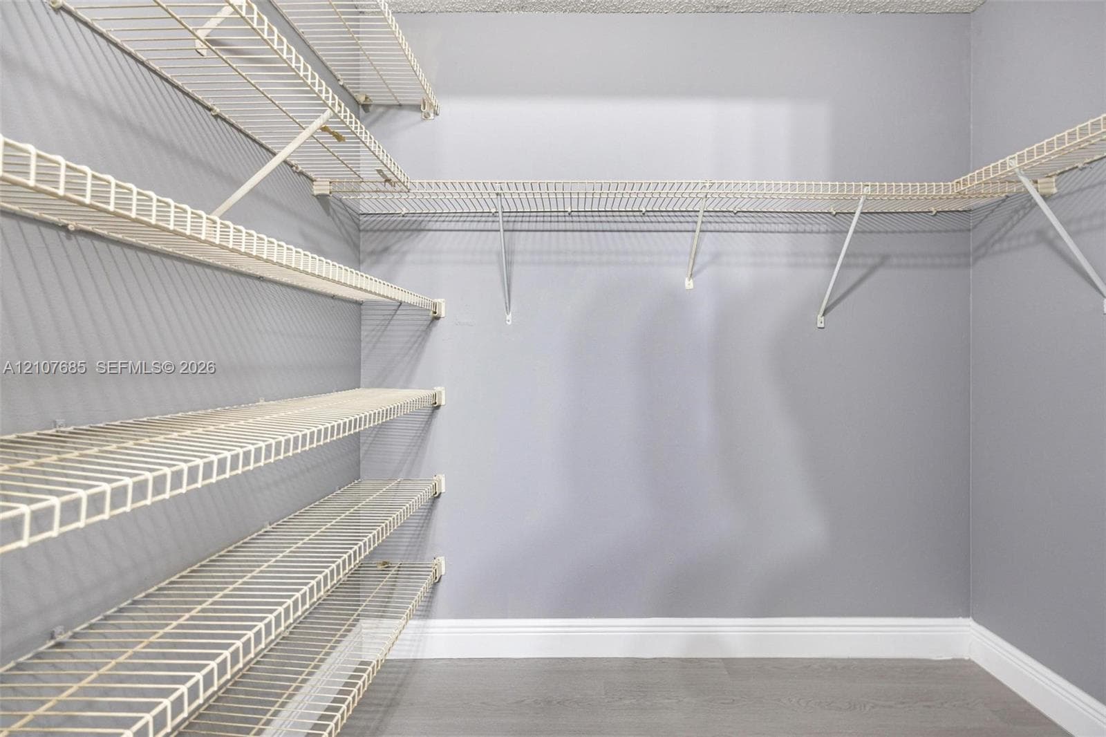 Walk-in storage space featuring multi-tiered white wire shelving, neutral-toned walls, and wood-finish flooring