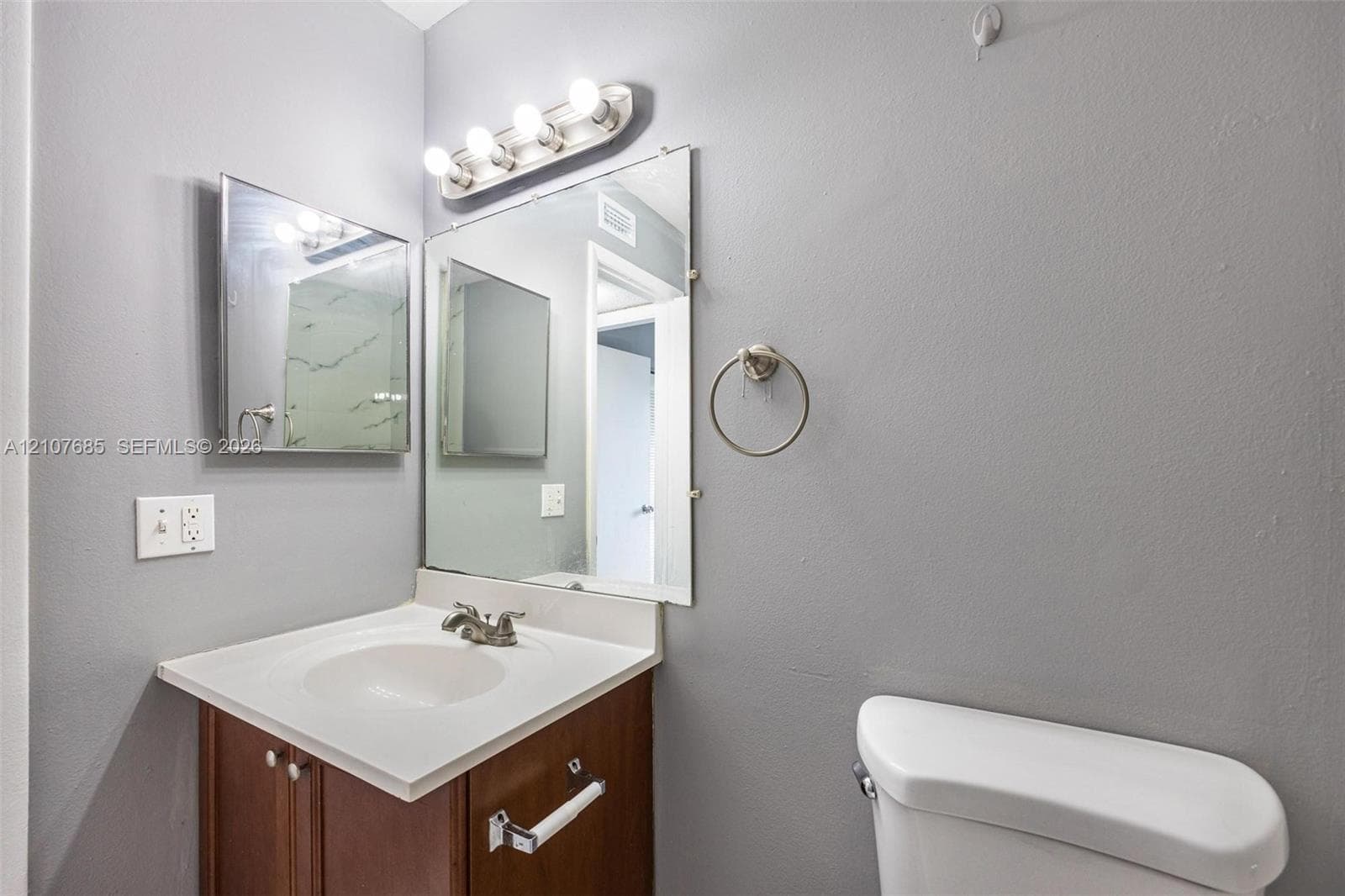 Vanity featuring a solid-surface integrated sink, wood-finish cabinetry, a large frameless mirror, and a four-light fixture