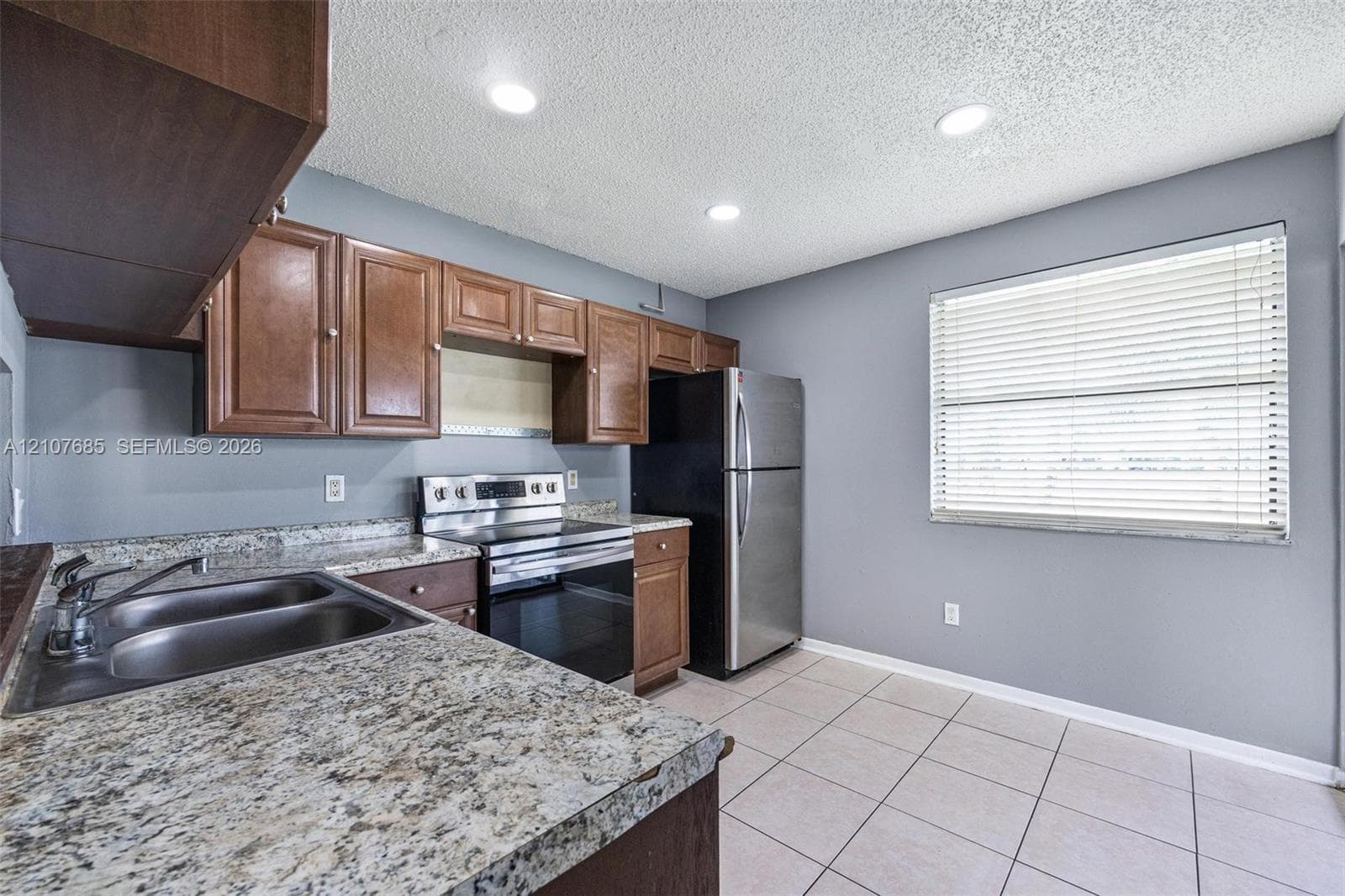 Kitchen featuring wood cabinetry, stone-finish countertops, dual-basin stainless steel sink, stainless steel range, and tile flooring