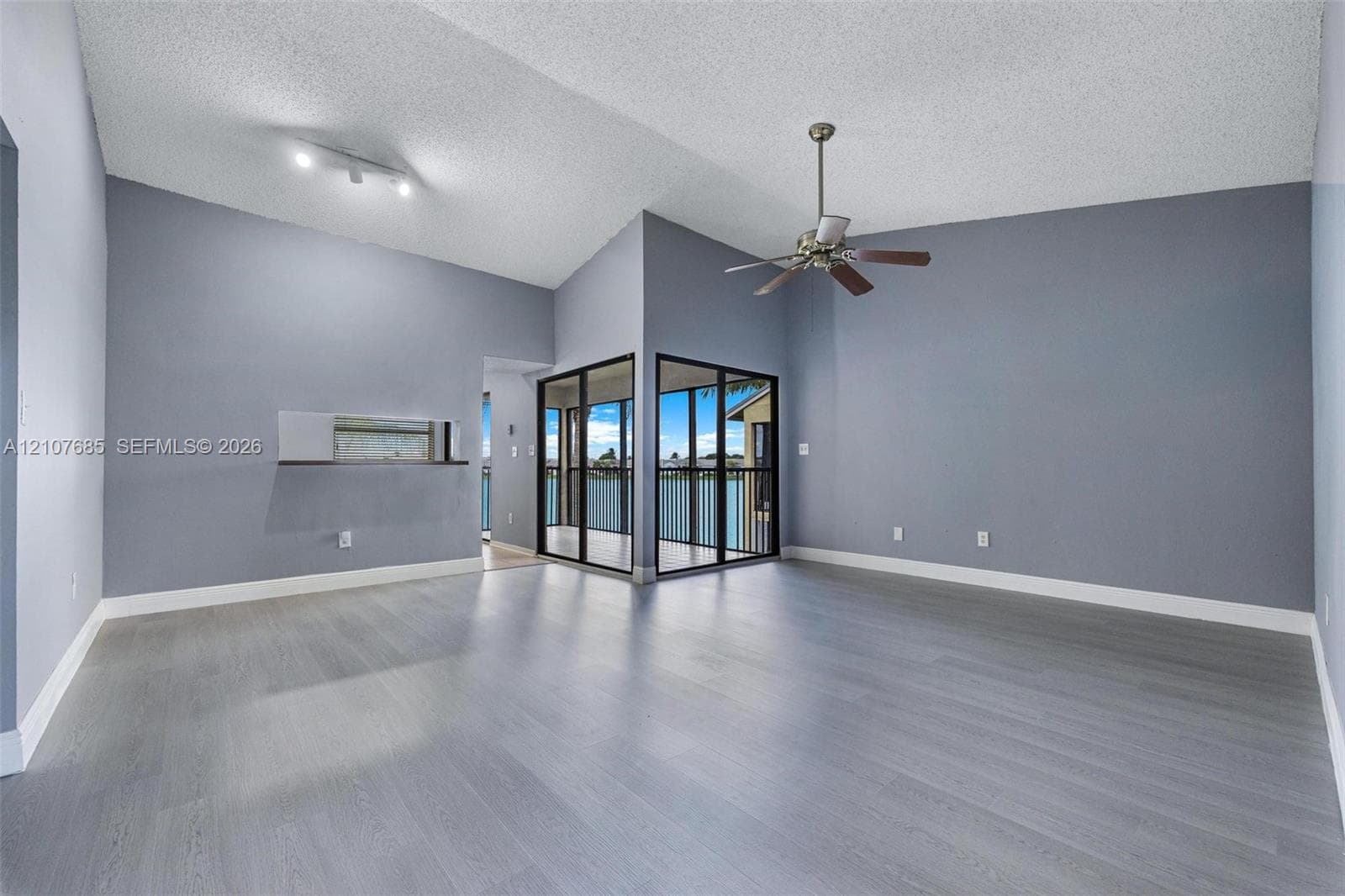 Vaulted ceilings, wood-finish flooring, ceiling fan, pass-through wall opening, and floor-to-ceiling glass enclosure