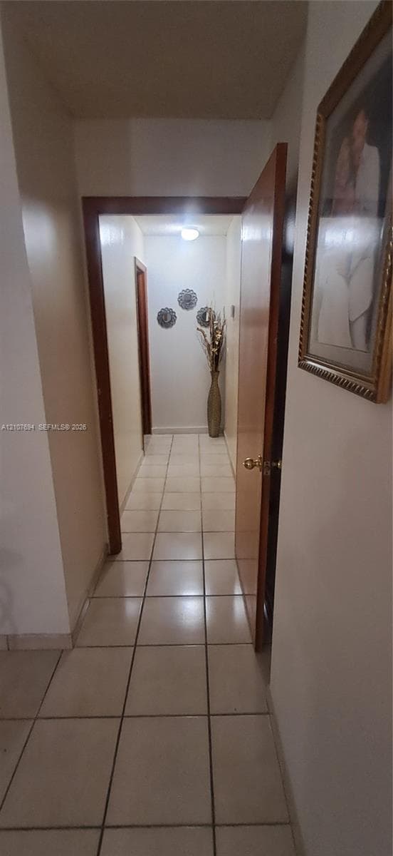 Hallway featuring large-format ceramic tile flooring, solid wood-finish door frames, and a flush-mount ceiling light fixture