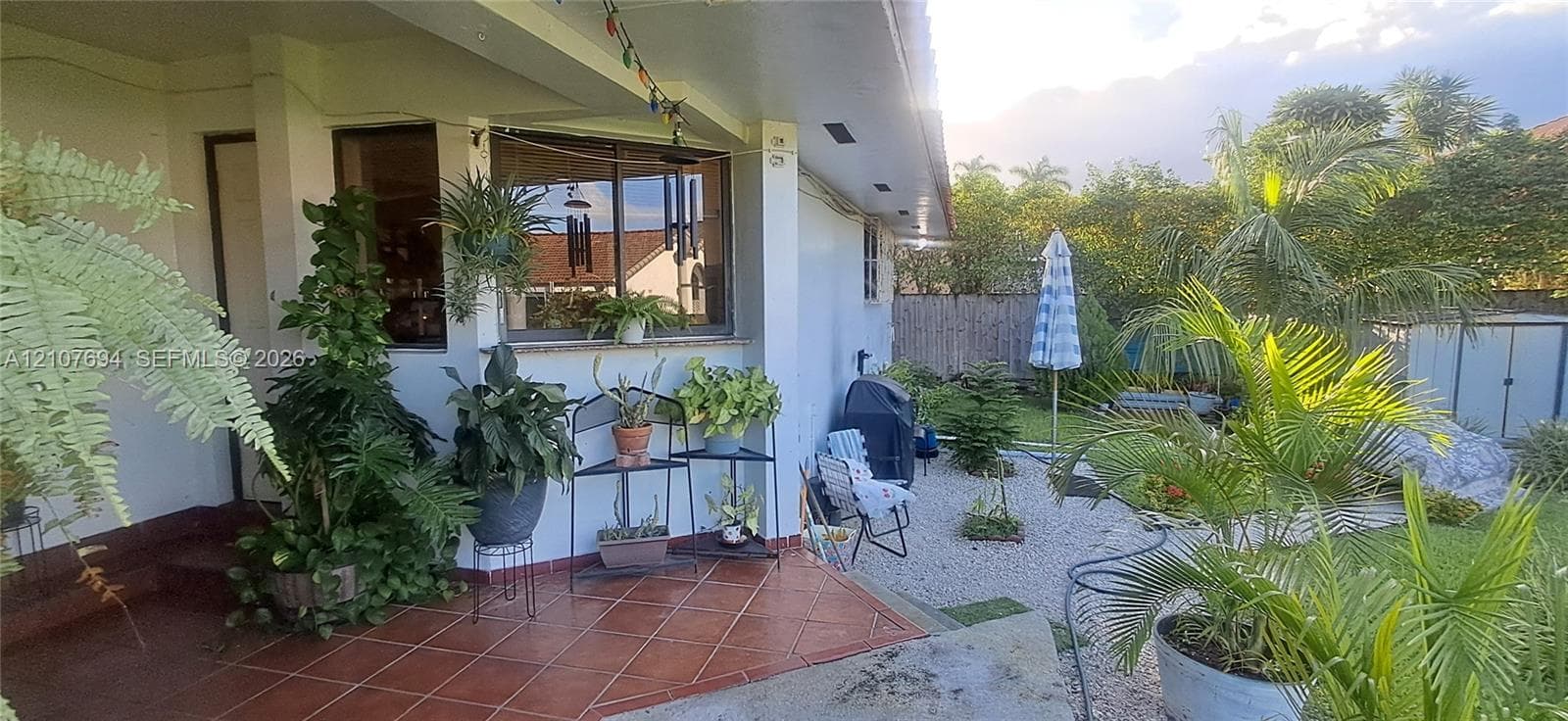 Covered patio featuring terracotta-style tile flooring, gravel ground cover, and mature exterior landscaping