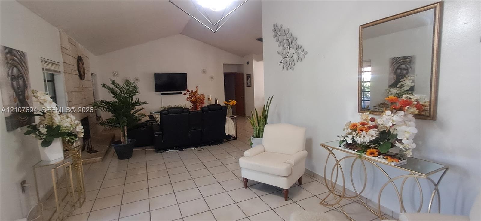Living area featuring vaulted ceilings, light-toned ceramic tile flooring, and a floor-to-ceiling natural stone fireplace