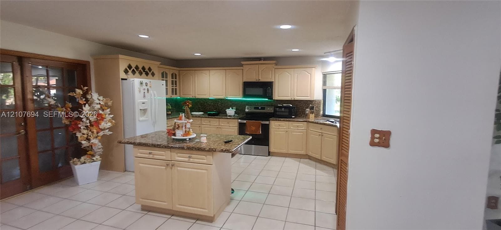 Kitchen featuring light-toned cabinetry, stone-surfaced countertops, a center island with built-in storage, tile flooring, and recessed lighting