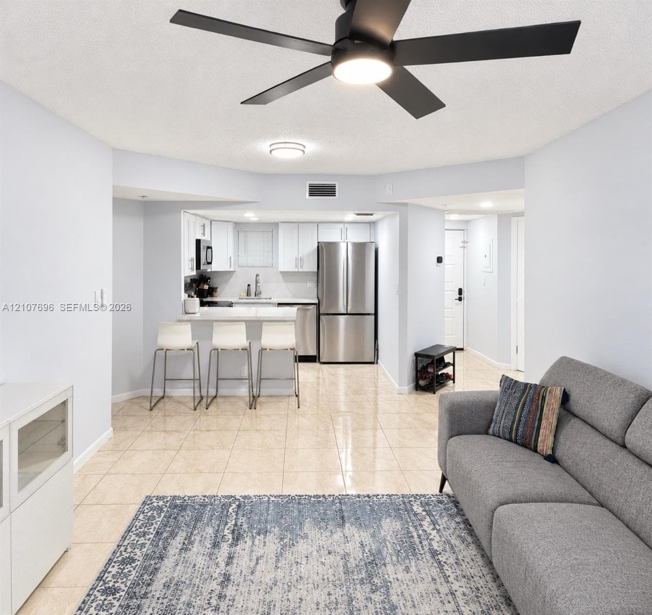 Living area featuring neutral tile flooring, a matte black ceiling fan, and a large sliding glass door providing natural light