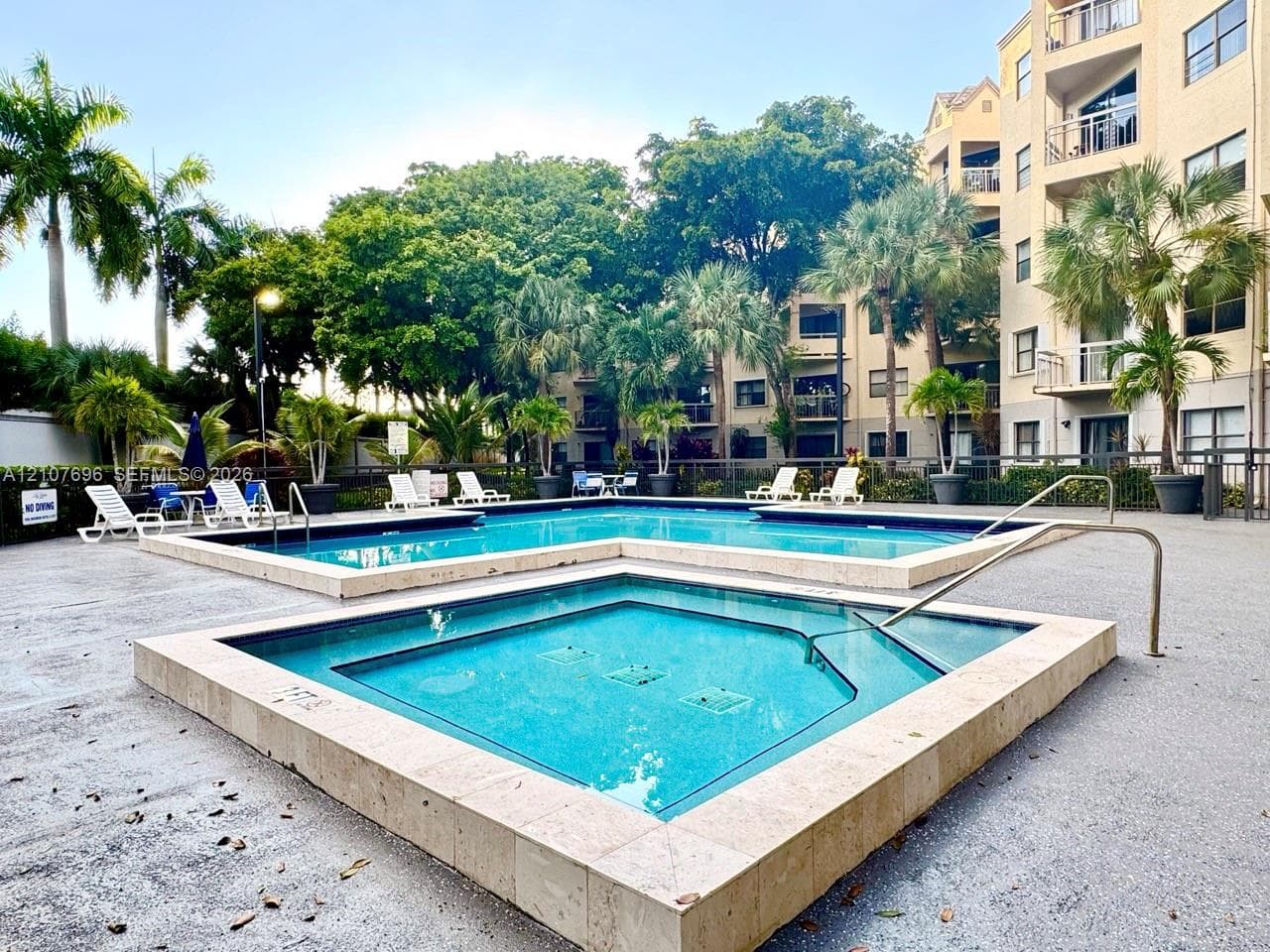 Multi-story exterior featuring a central peaked porte-cochere, expansive exterior balcony railings on each level, and integrated tropical landscaping