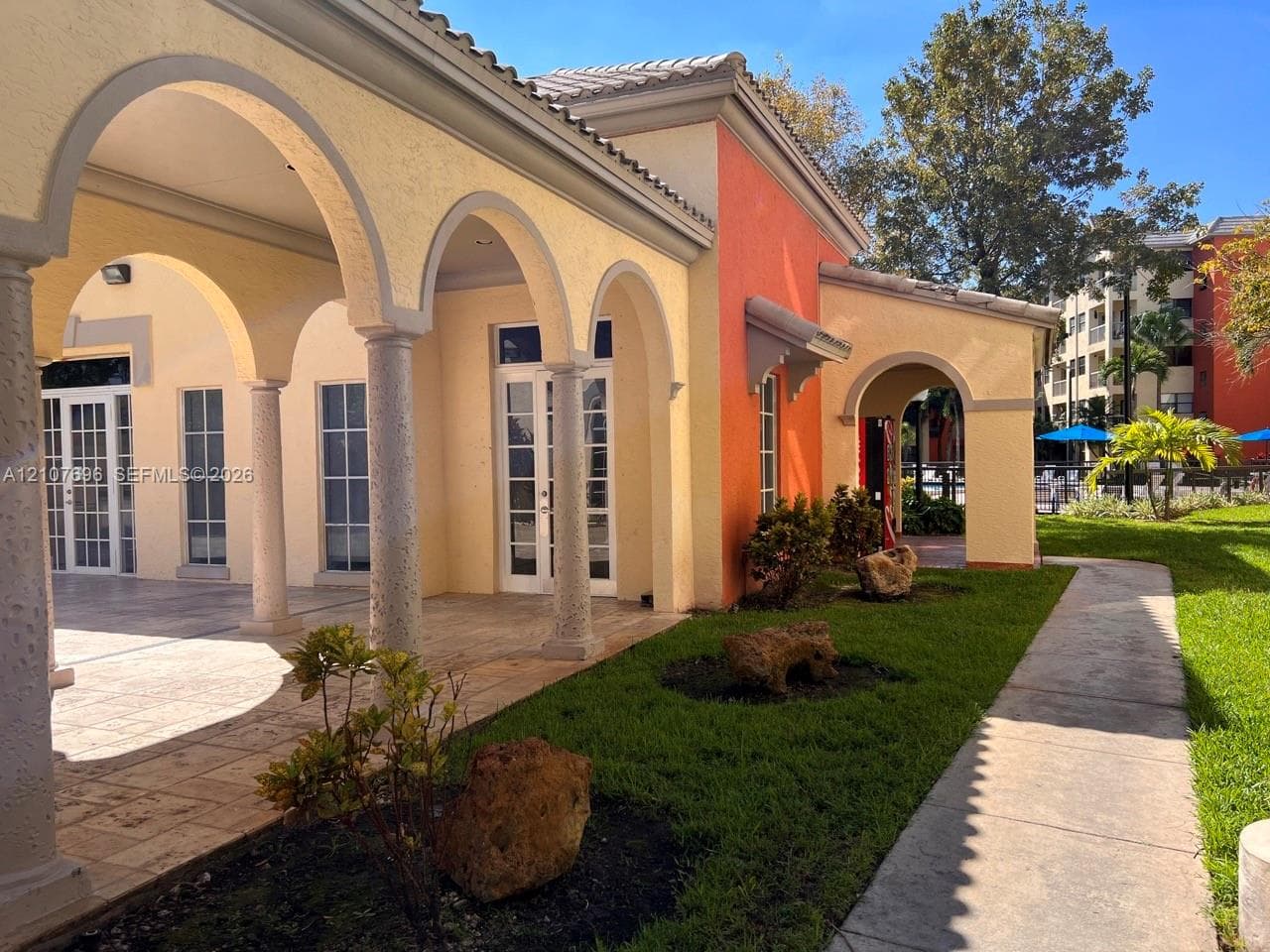 Multi-story building featuring private exterior balconies, paved surface parking, and mature trees