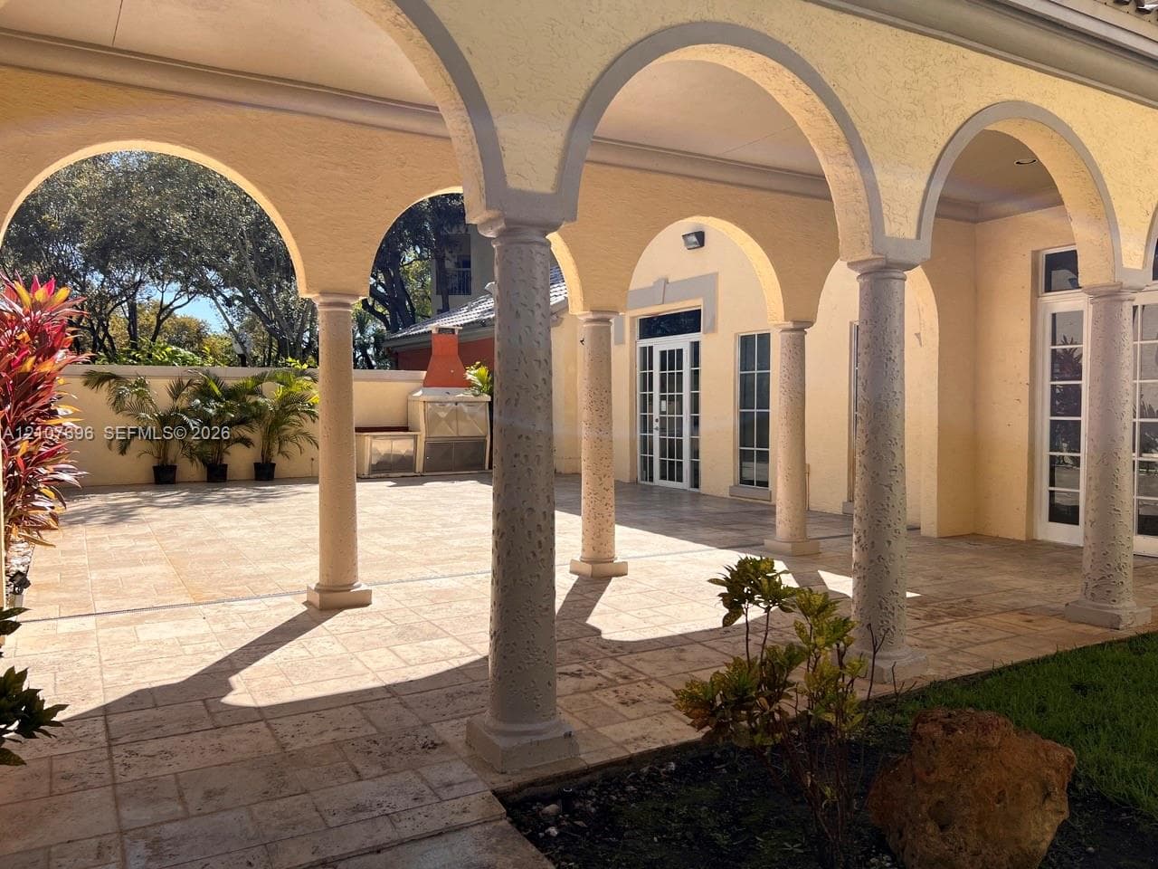 Stucco exterior building featuring arched entryways, dual French doors with glass panes, decorative window shutters, and a semi-circular attic vent