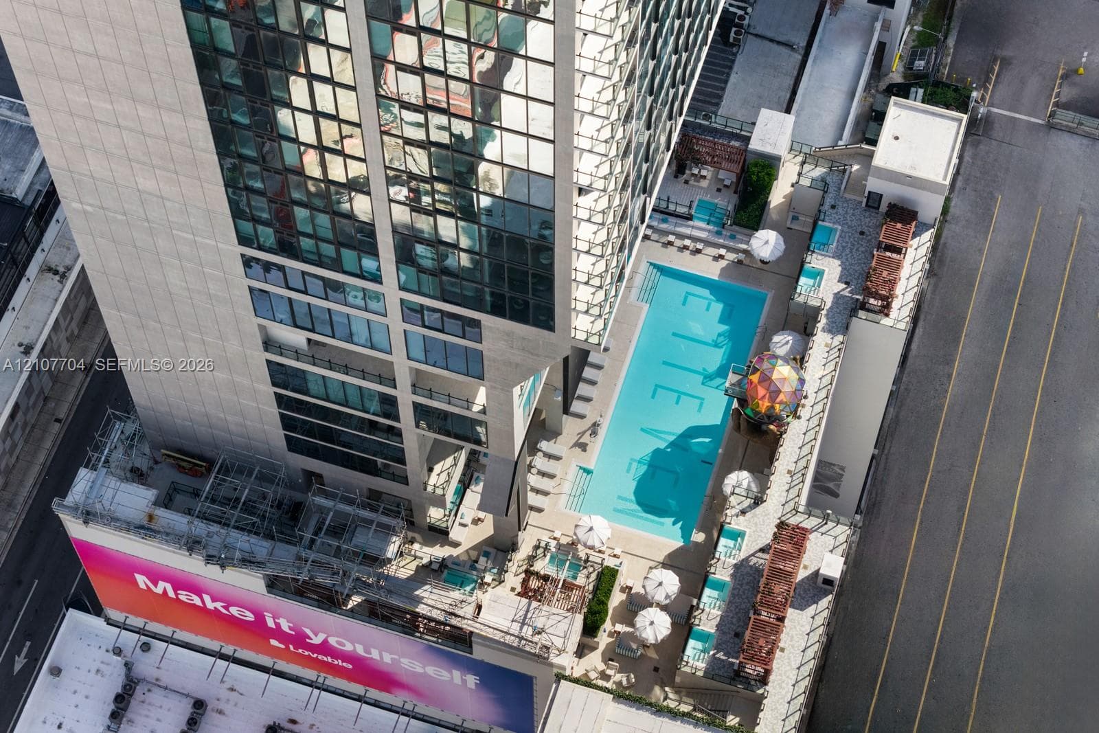Aerial perspective of high-rise structure featuring an outdoor swimming pool, paved sundeck, elevated terrace space, and glass-facade exterior