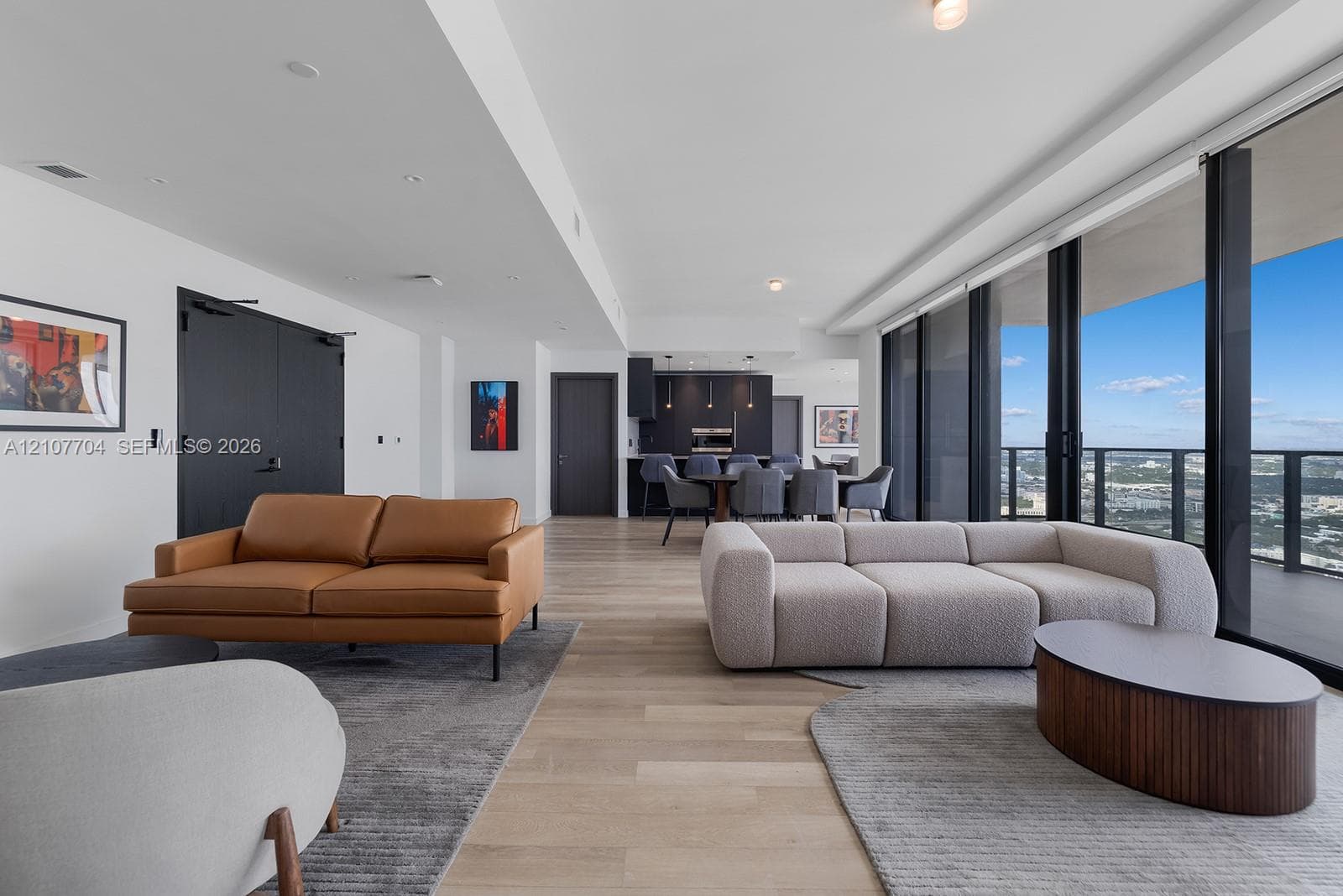 Open-concept living space featuring wood-finish flooring, floor-to-ceiling glass wall, recessed lighting, and kitchen cabinetry with integrated appliances