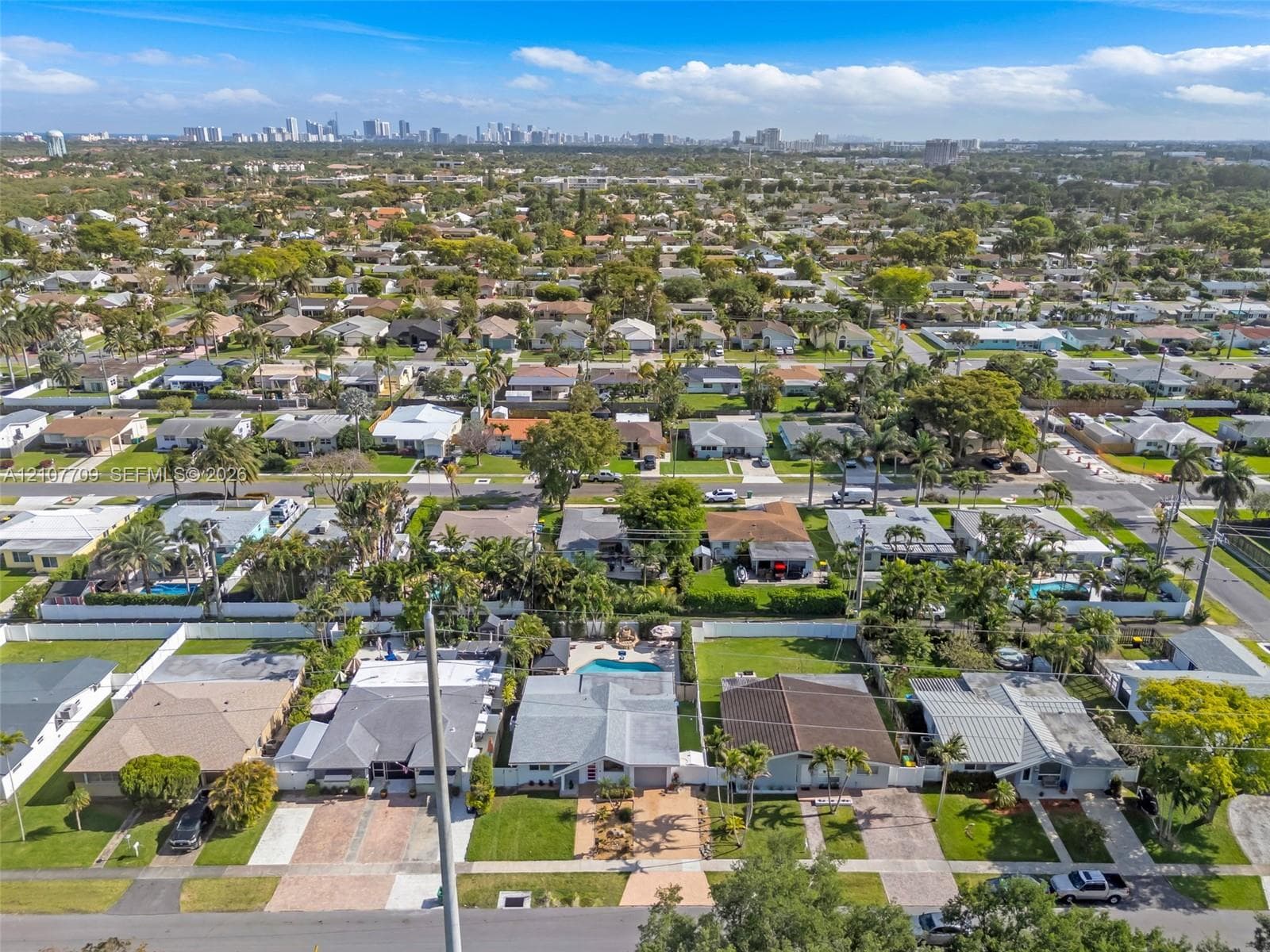 Aerial perspective featuring established residential landscaping, paved driveways, concrete-tile roofing, fenced perimeters, and a distant city skyline