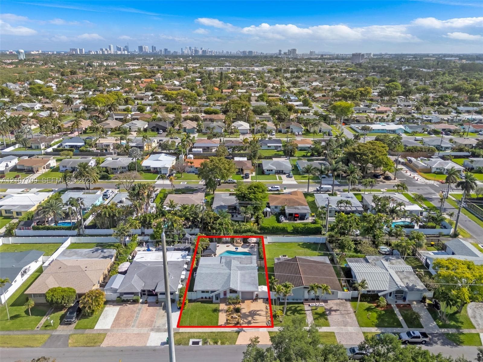 Aerial perspective featuring a single-story residence with a concrete-tile roof, expansive front lawn, paved driveway, and private backyard pool