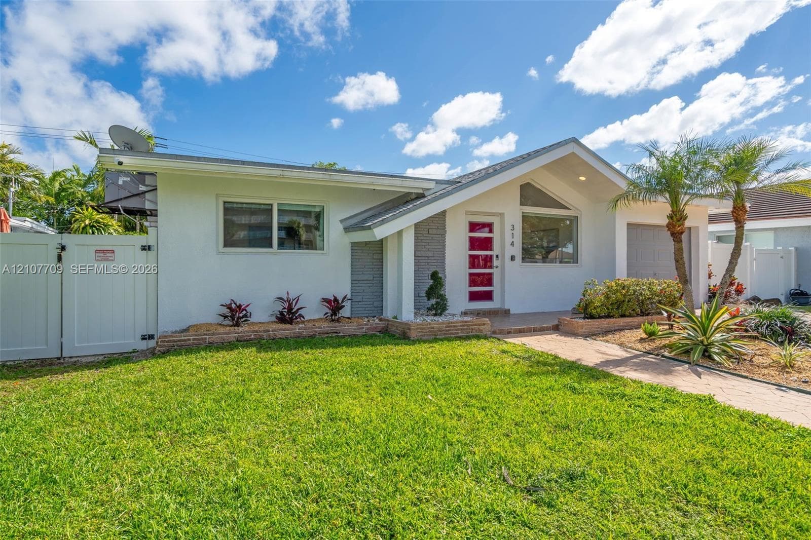 Single-story residence featuring a mid-century inspired roofline, white exterior finish with textured stone accents, a multi-pane red entry door, and a paved walkway leading to the home