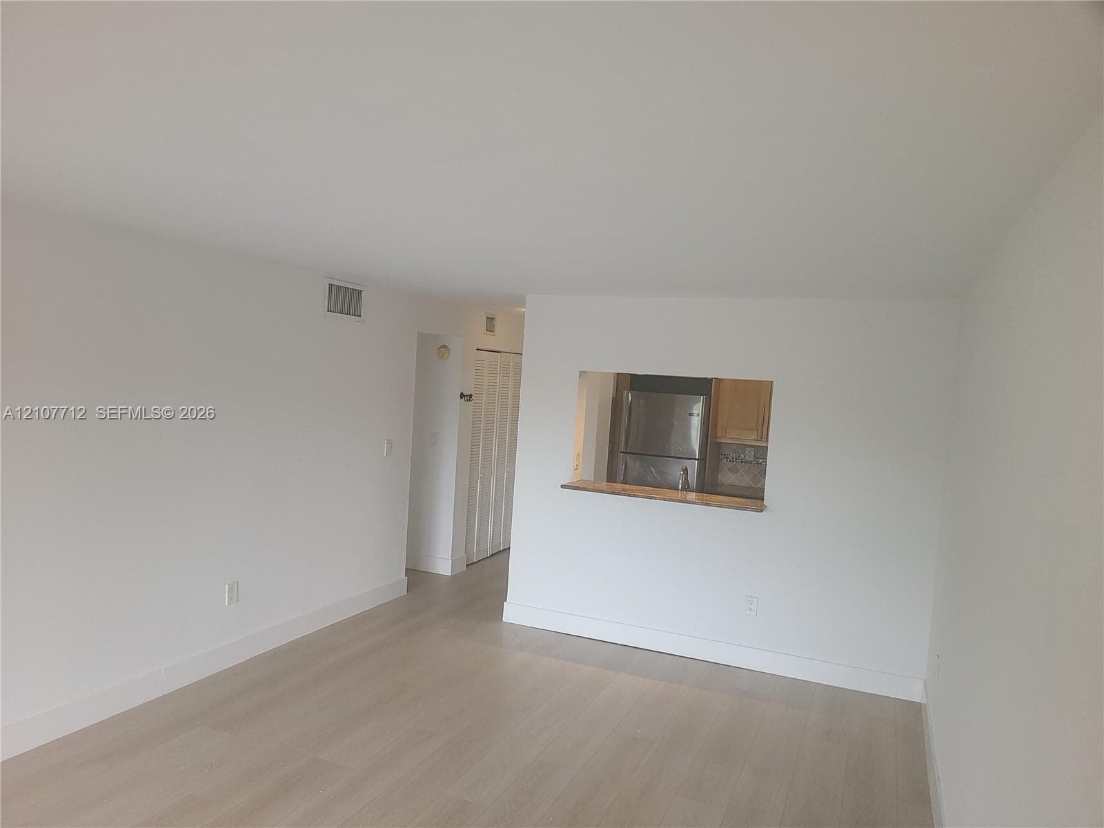 Interior featuring light-toned wood-finish flooring, a pass-through opening to the kitchen, and bifold closet doors