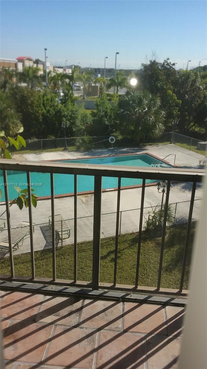 Covered balcony featuring tile flooring and a metal railing overlooking an in-ground swimming pool with concrete decking and perimeter fencing