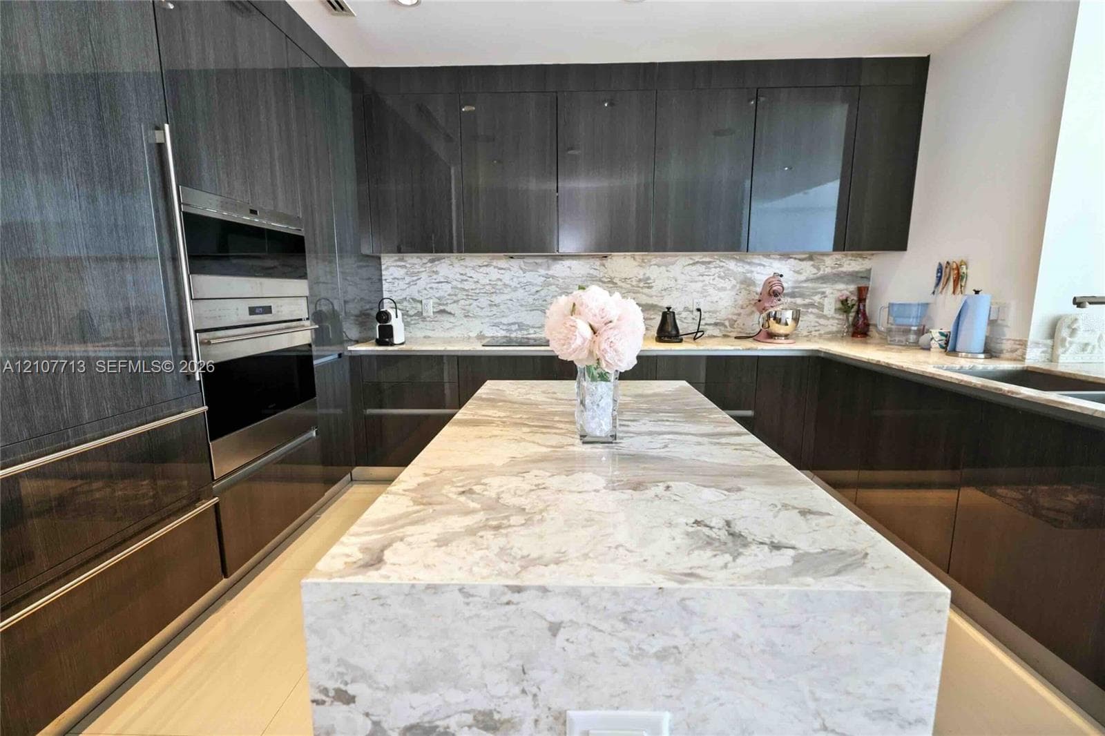 Modern kitchen featuring high-gloss cabinetry, stone countertops with waterfall-edge island, built-in stainless steel wall oven, and built-in microwave