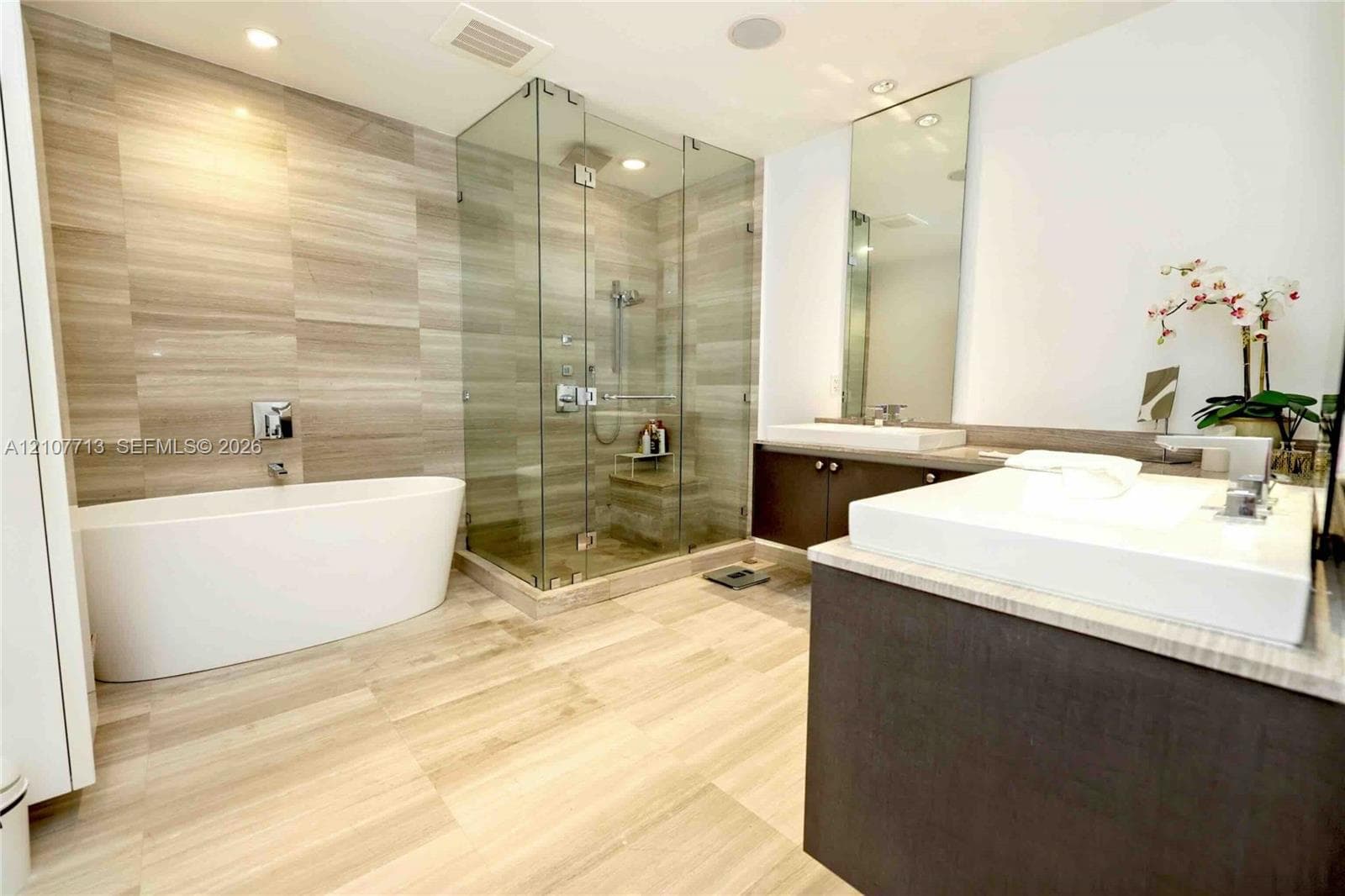Freestanding soaking tub, glass-enclosed walk-in shower with tiled surround, dual-sink vanity with solid-surface countertops, and oversized wall mirror
