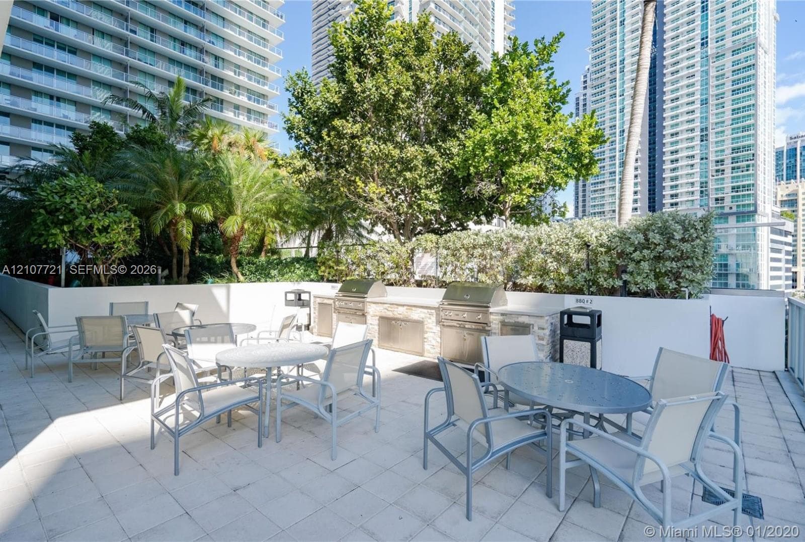 Outdoor terrace featuring stone-tiled flooring, a built-in stainless steel dual-grill station, and perimeter shrubbery