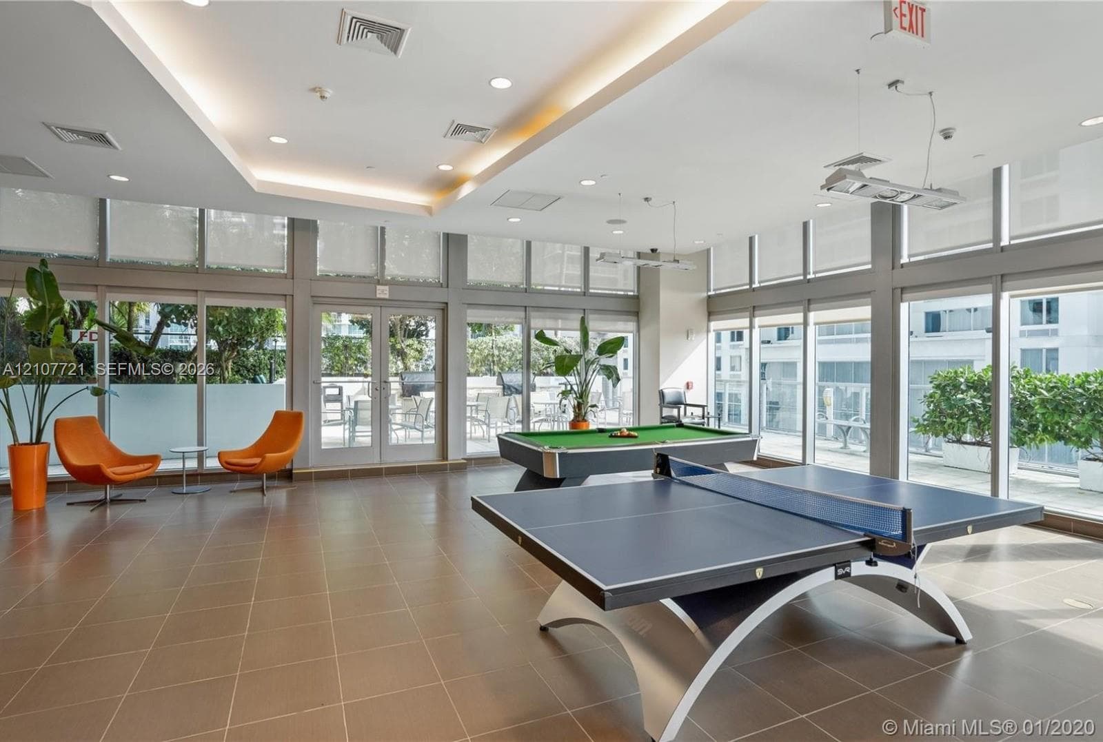 Spacious recreation room featuring tile flooring, recessed tray ceiling lighting, and floor-to-ceiling windows