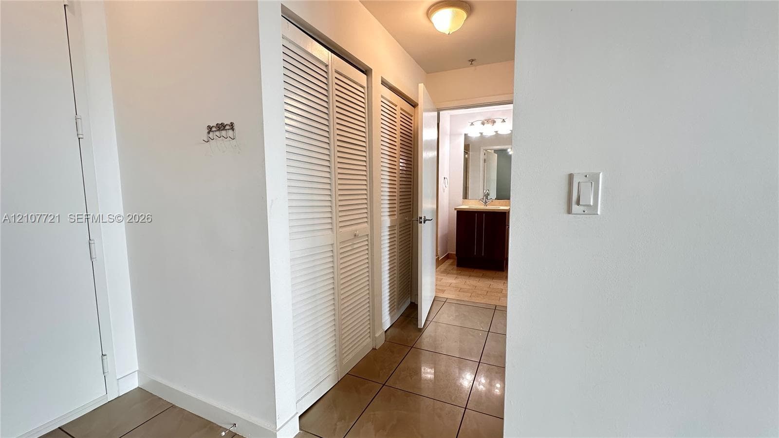 Hallway featuring dual white louvered closet doors, tiled flooring, and a flush-mount ceiling light fixture