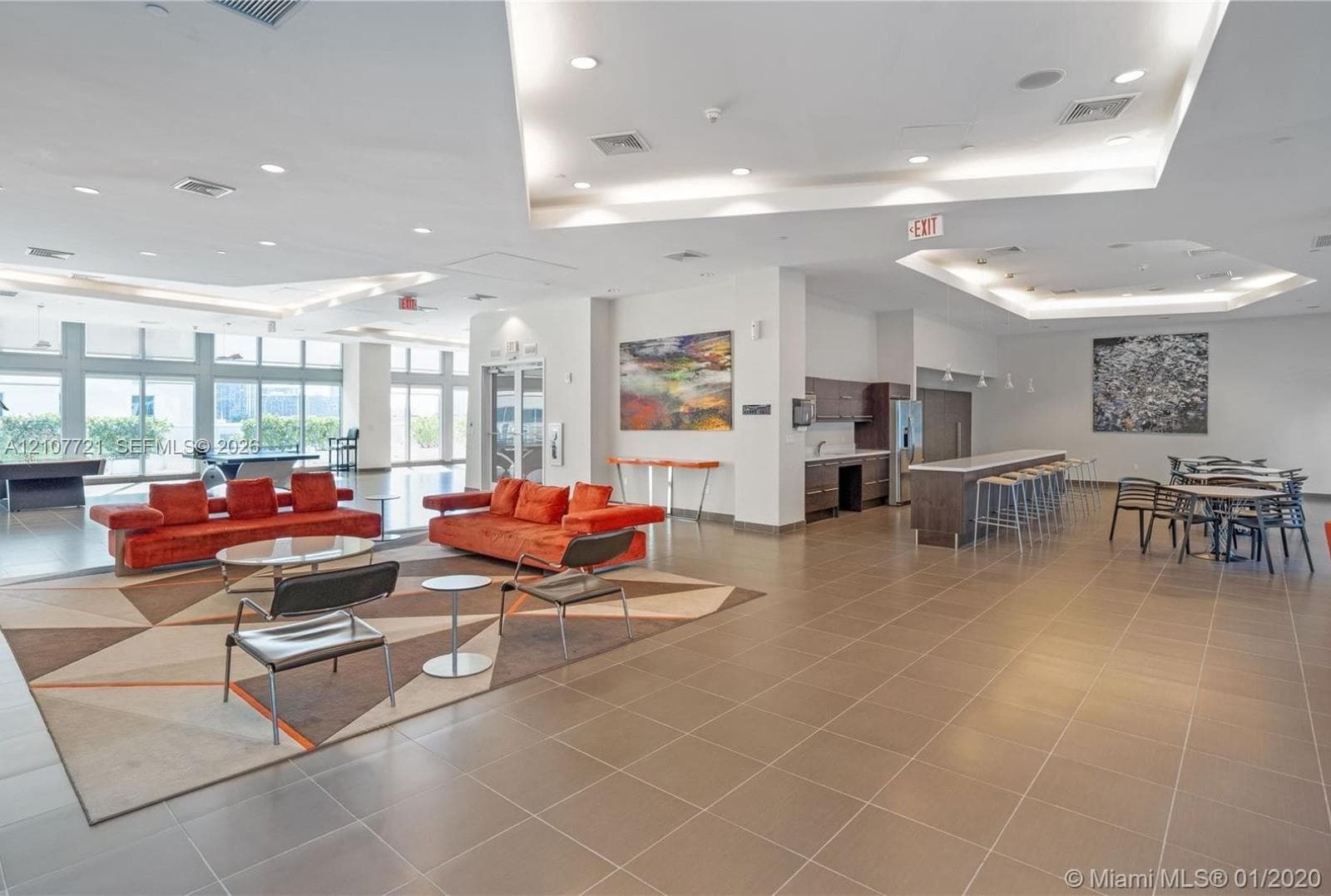 Open-concept common area featuring recessed tray ceilings, oversized ceramic floor tiling, floor-to-ceiling windows, and a built-in kitchenette with a stone-top breakfast bar