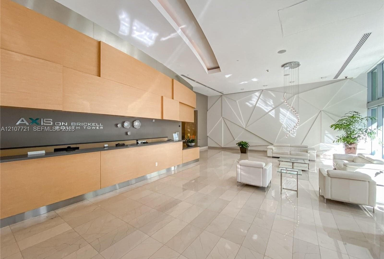 Contemporary lobby featuring floor-to-ceiling wood-paneled reception desk, geometric wall detailing, large-format tile flooring, and a spiral pendant light fixture