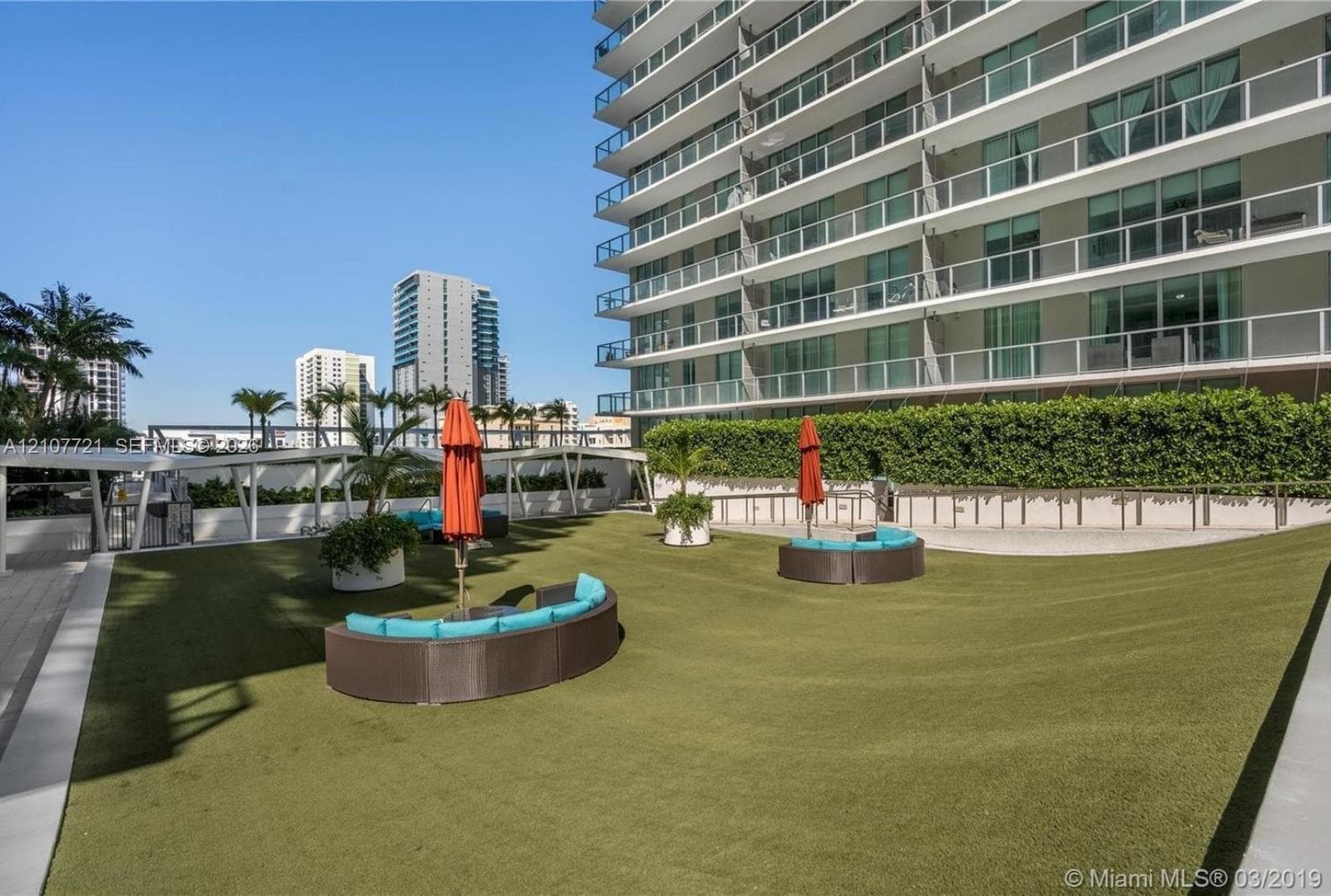 Elevated terrace featuring synthetic turf, structured perimeter hedging, and stone-tile pathways