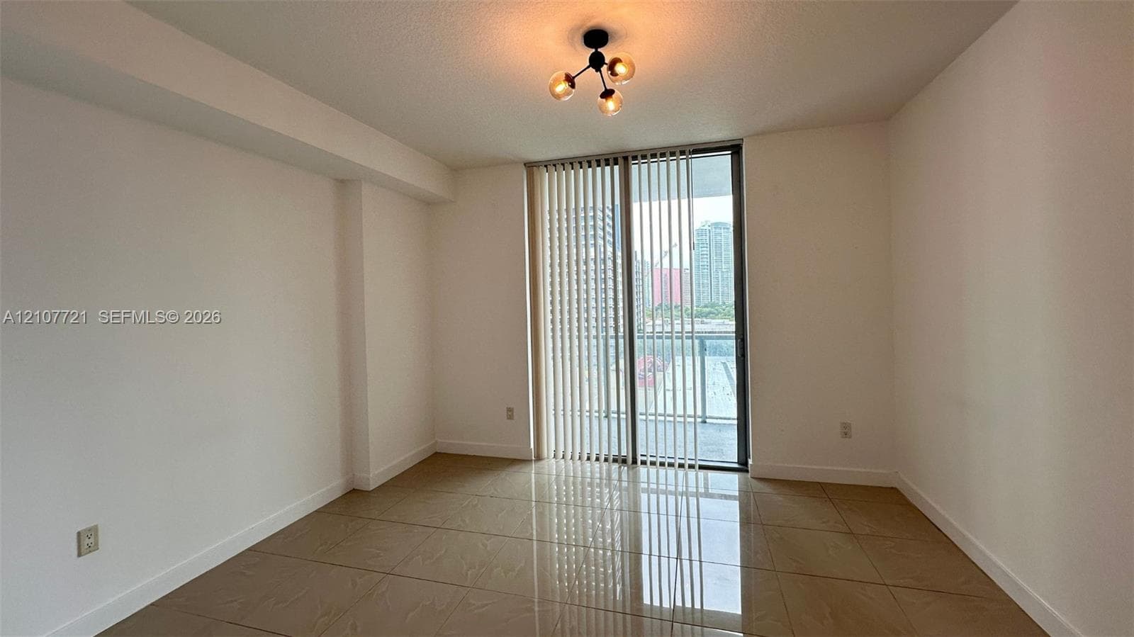 Interior room featuring neutral wall finishes, large-format tile flooring, a modern three-light branching chandelier, and floor-to-ceiling glass sliding doors opening to an exterior balcony