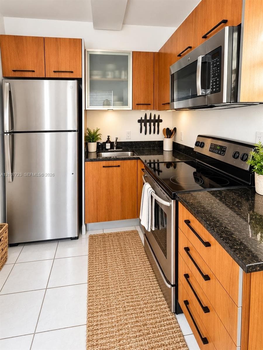 Kitchen featuring wood-finish cabinetry, stainless steel appliances, dark stone-style countertops, an upper glass-front cabinet, and tile flooring