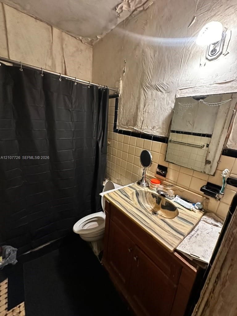 Vanity cabinet with a stone-finish countertop and integrated sink, wall-mounted light fixture, square wall tiling with decorative border, and a rectangular mirror