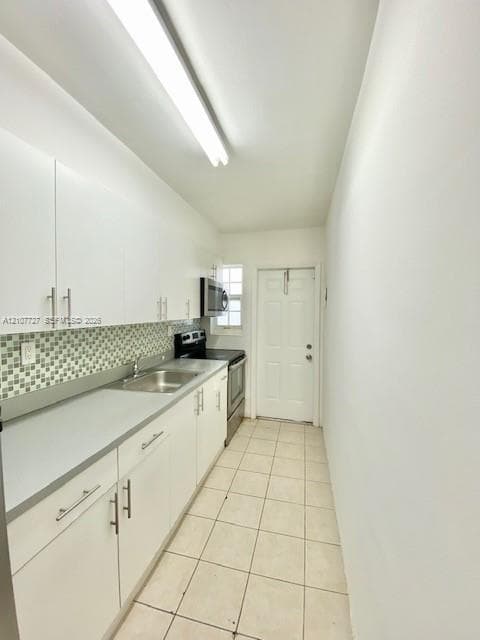 Kitchen featuring white cabinetry with brushed metal hardware, solid-surface countertops, mosaic tile backsplash, integrated stainless steel sink, and ceramic tile flooring
