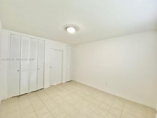 Room interior featuring neutral tile flooring, white walls, flush-mount ceiling lighting, and multiple floor-to-ceiling closets with white louvered bi-fold doors