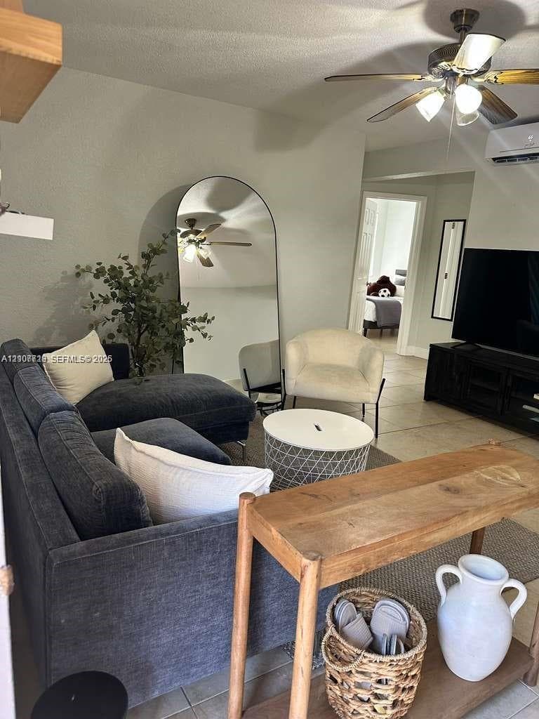 Living area featuring large-format tile flooring, arched wall detailing, a ceiling fan with integrated lighting, and a wall-mounted ductless mini-split air conditioning unit