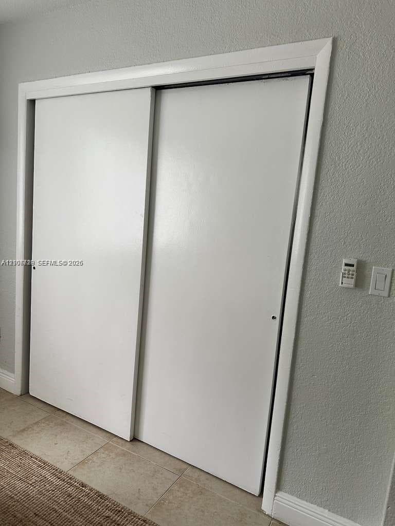 Sliding closet doors featuring white panels, neutral textured wall finish, and neutral tile flooring