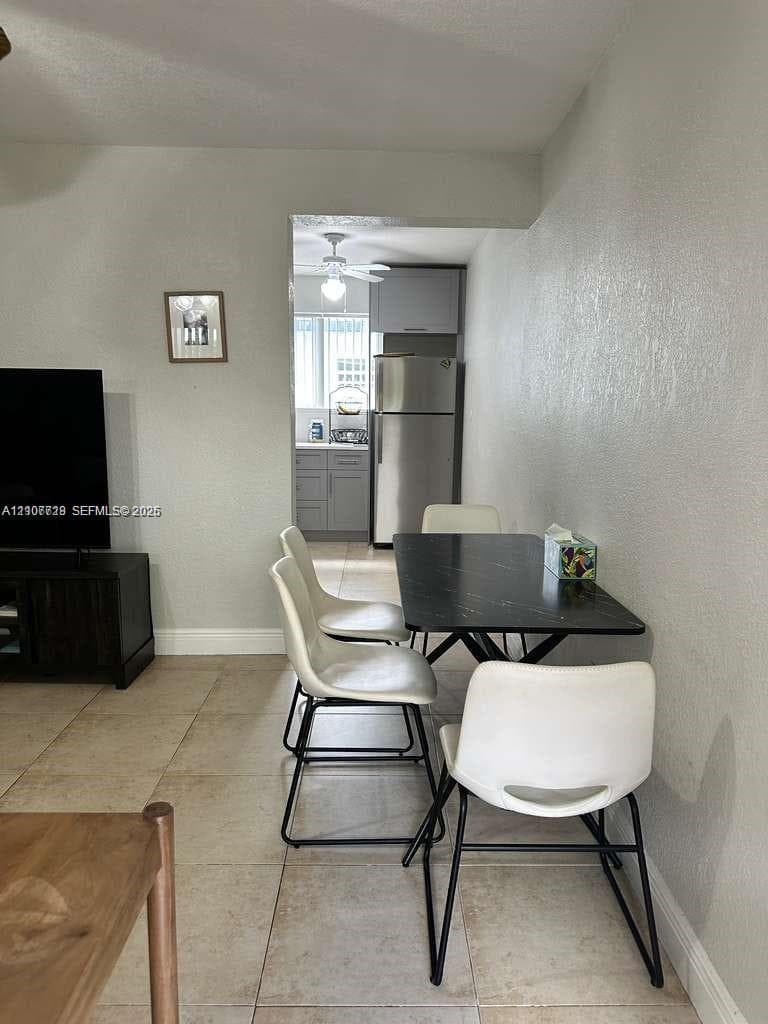 Neutral-tone tile flooring, textured wall finishes, and integrated kitchen featuring stainless steel refrigerator and gray cabinetry